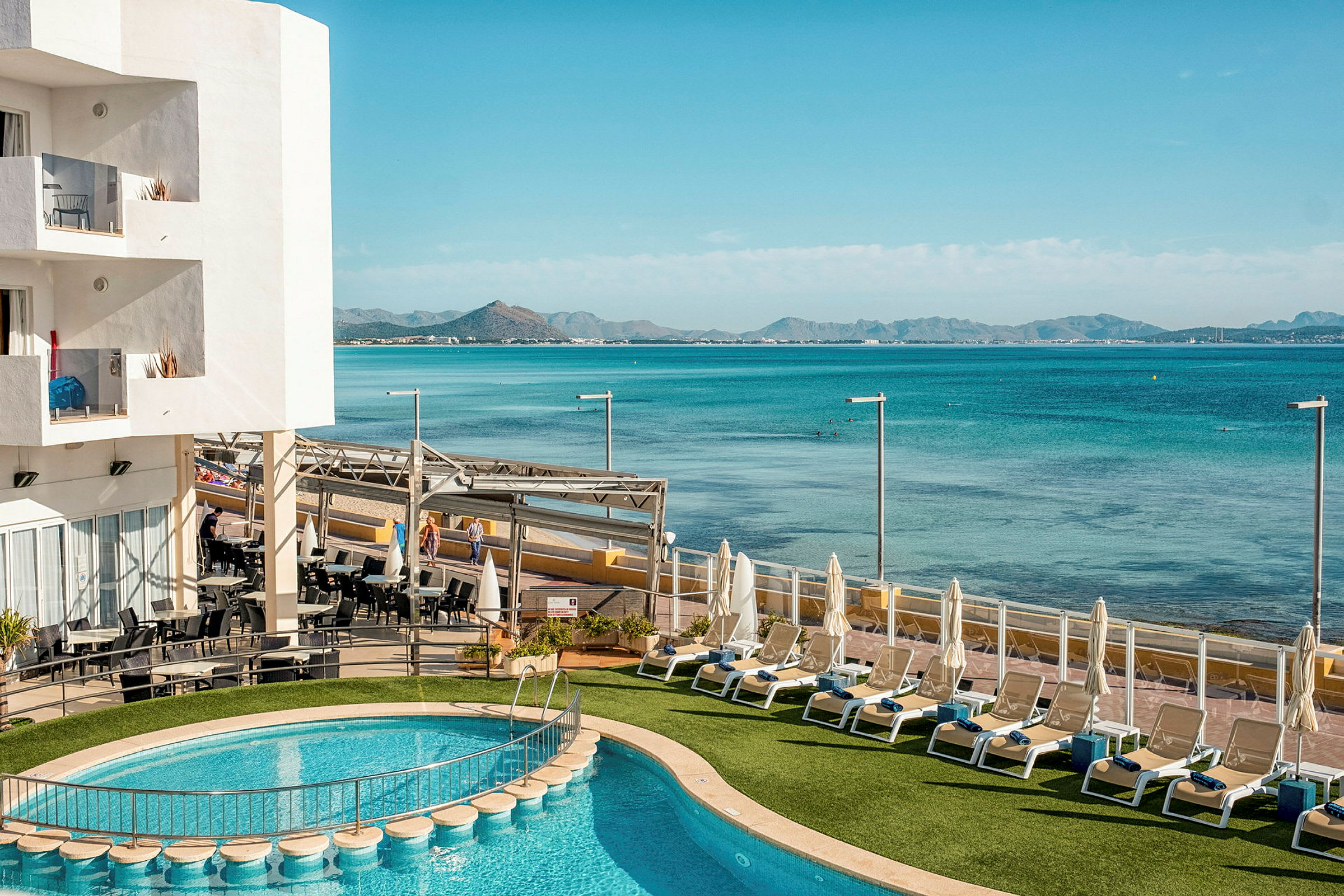 Bild föreställer en hotellpool med utsikt över havet och berg i bakgrunden. (AI-genererad text)