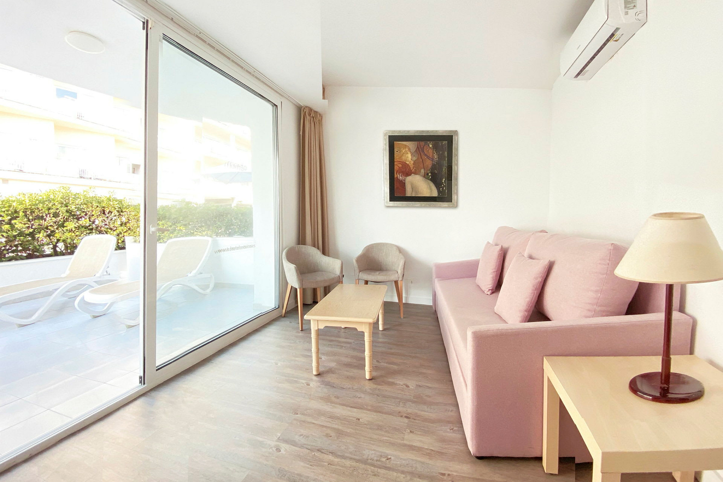 Soffa med rosa klädsel, vardagsrumsbord, två stolar och fönster med utsikt mot terrassen. (AI-genererad text)