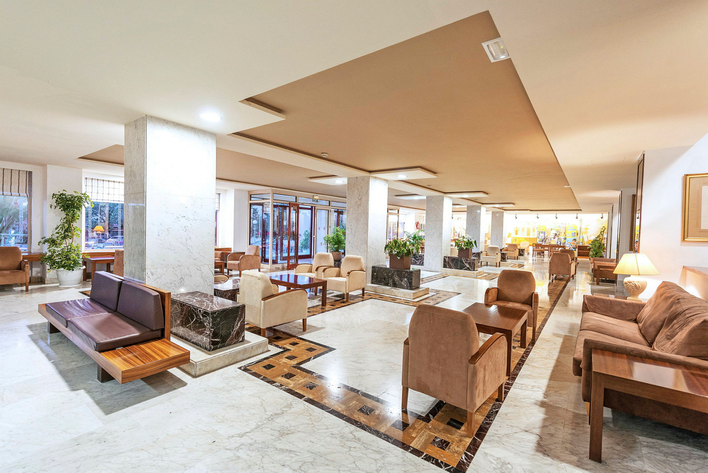 En rymlig hotellobby med sittgrupper, soffor och bord. Golvet är dekorerat med marmor. (AI-genererad text)