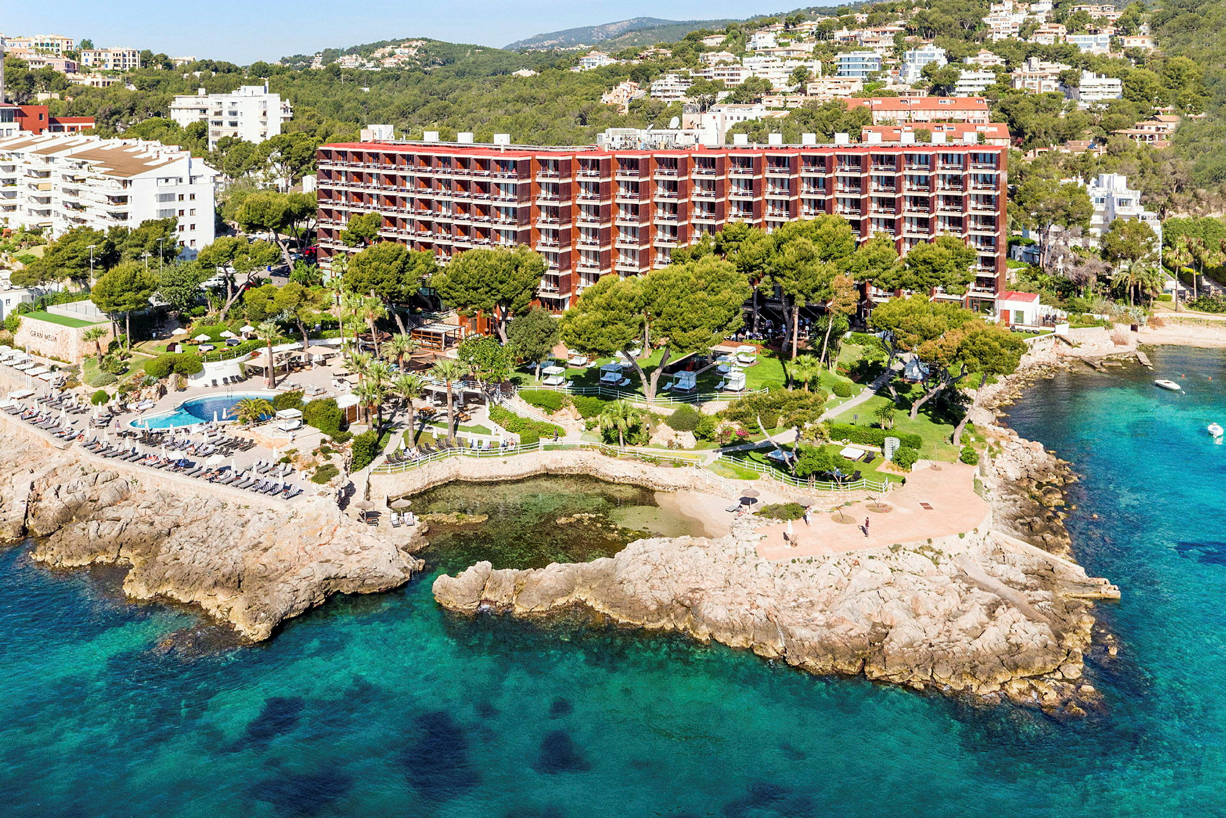 Flygfoto av en lyxresort vid havskusten med omgivande grönska och poolområden. (AI-genererad text)