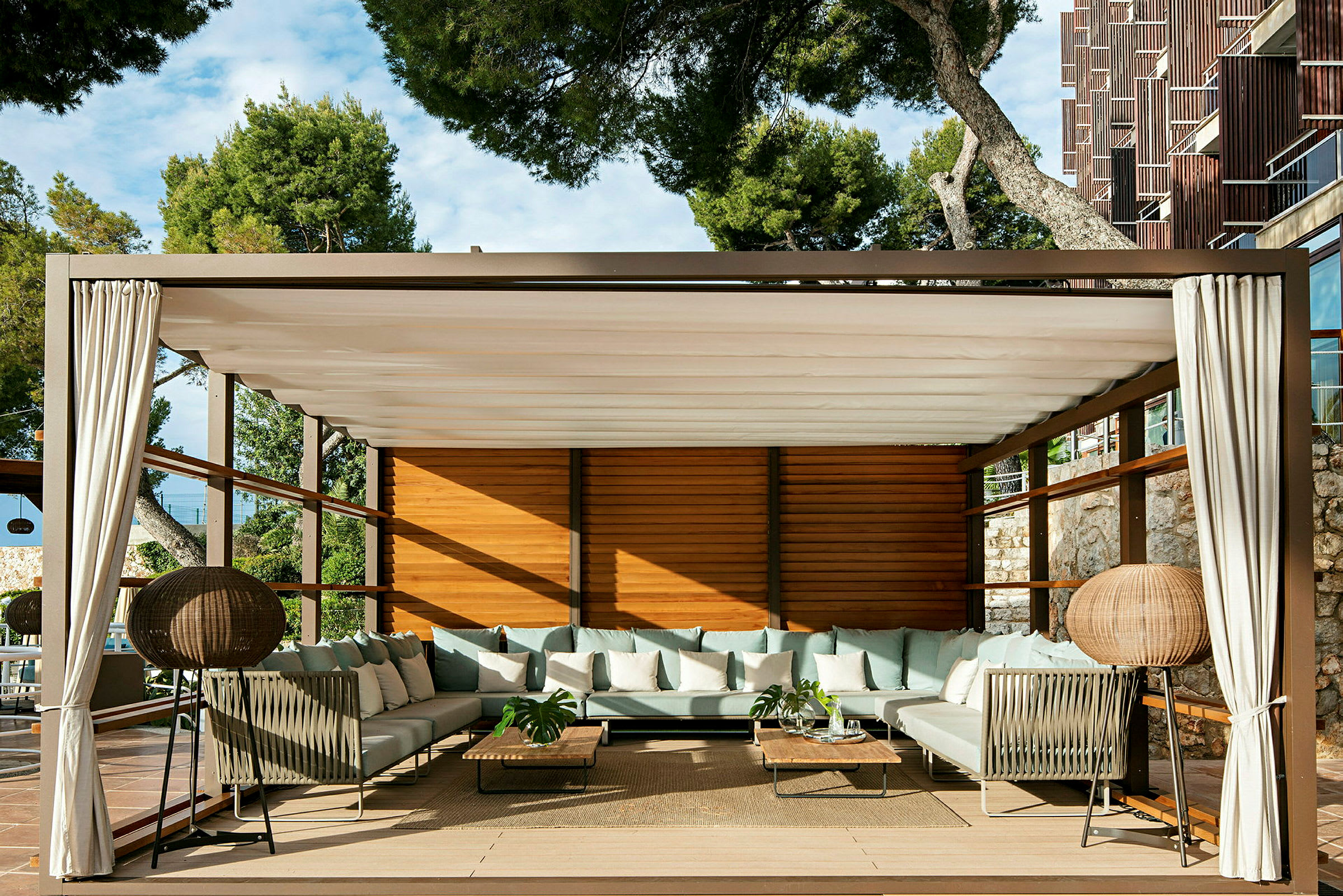 En lounge med soffor, bord och gardiner under en pergola. (AI-genererad text)