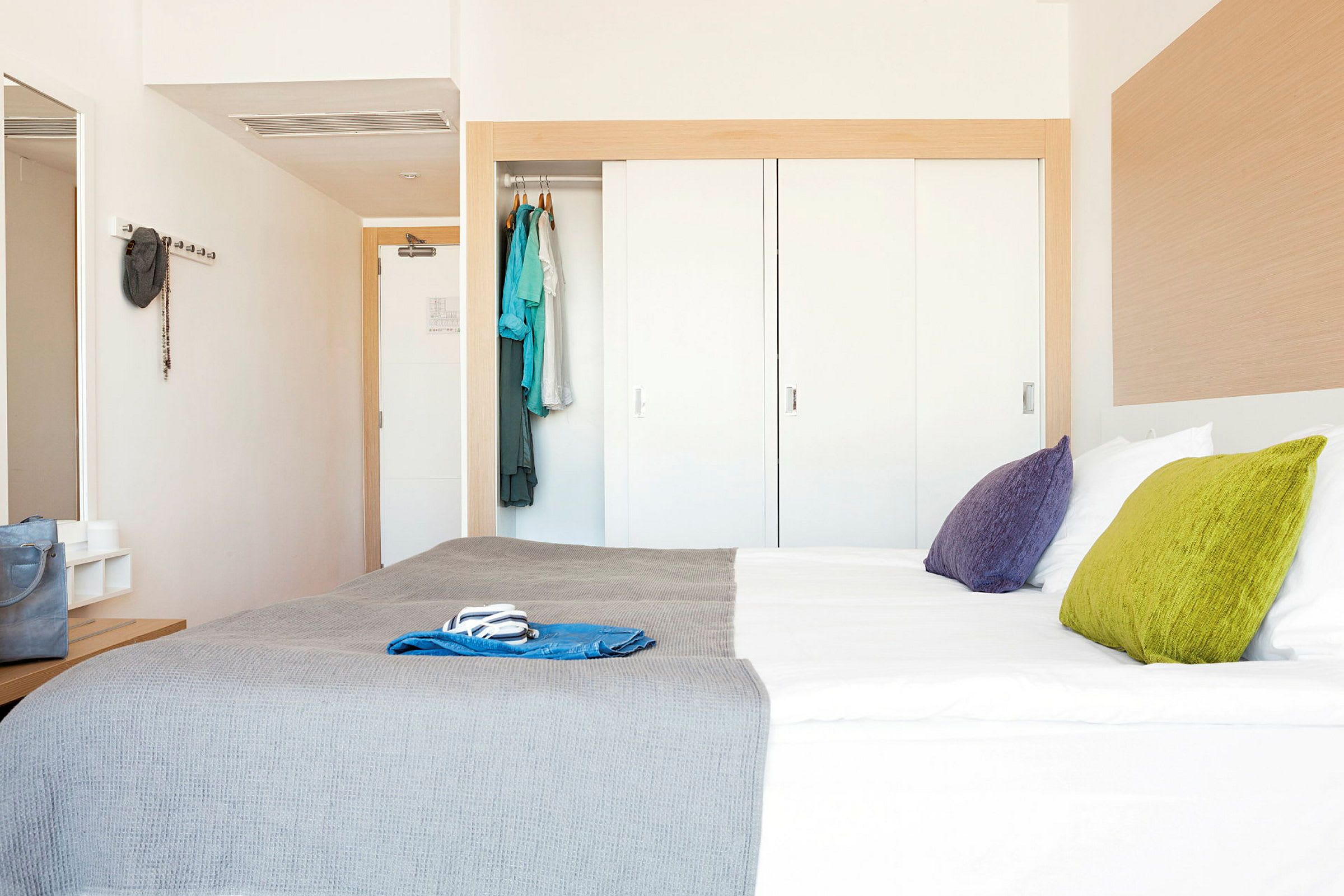 Ett hotellrum med en dubbelsäng, färgglada kuddar och en garderob. (AI-genererad text)