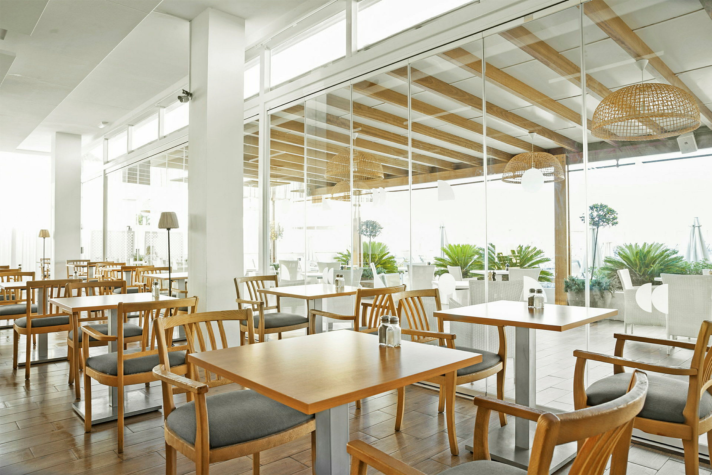 En restaurang med träbord och stolar, ljus inredning och stora glaspartier. (AI-genererad text)