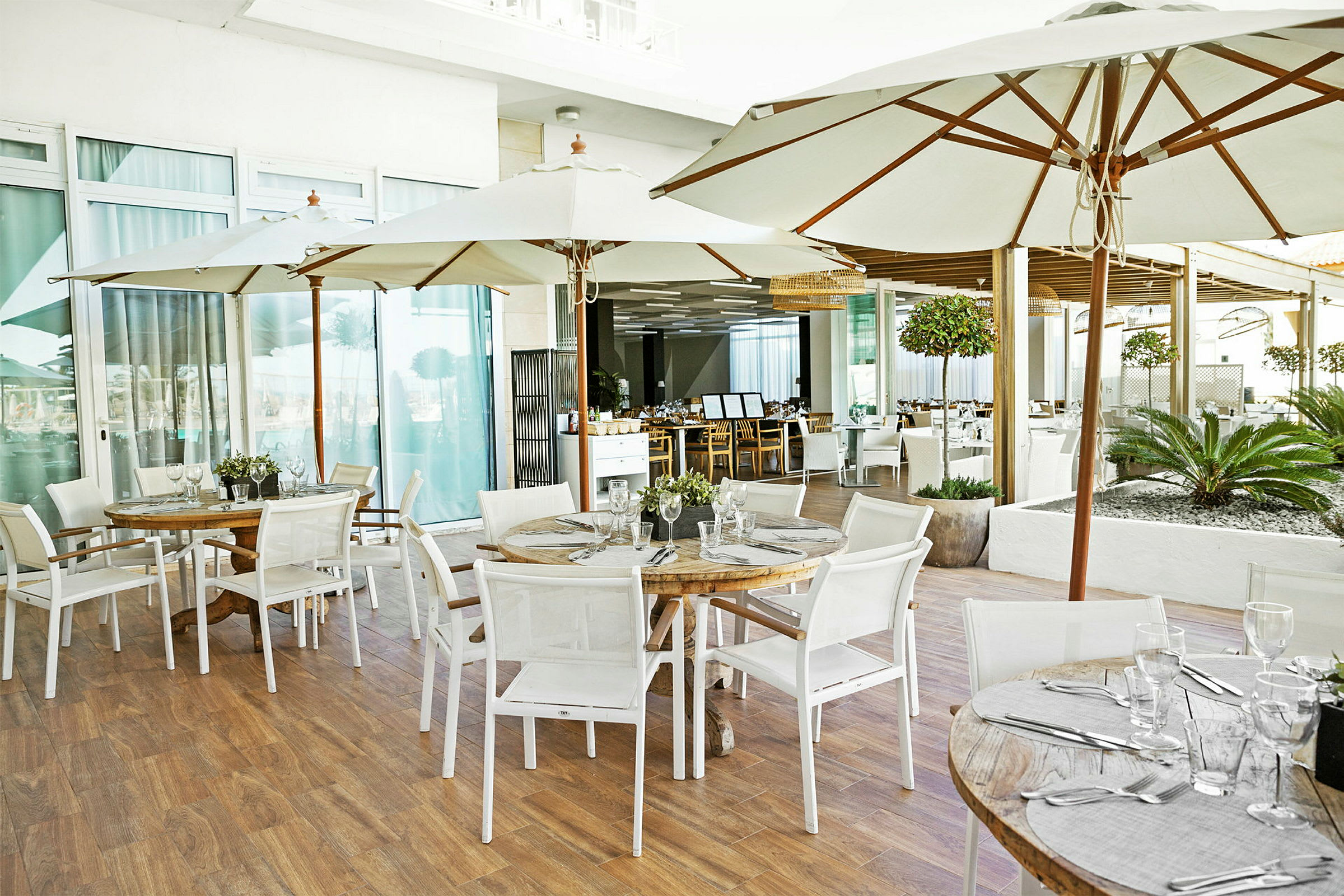 Bord med parasoller och stolar på en restaurangterrass. Glas och bestick är placerade på borden. (AI-genererad text)