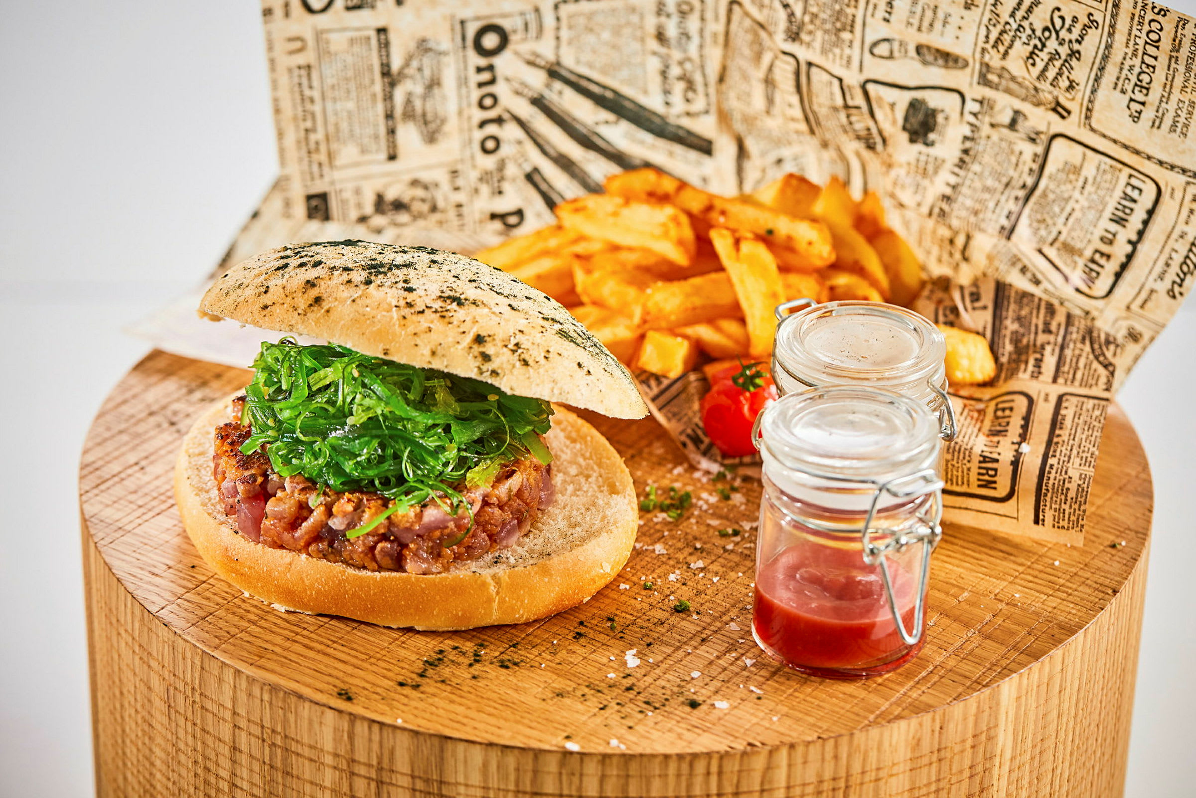 En hamburger med sallad på ett träbord tillsammans med pommes frites och glassburkar med sås. (AI-genererad text)