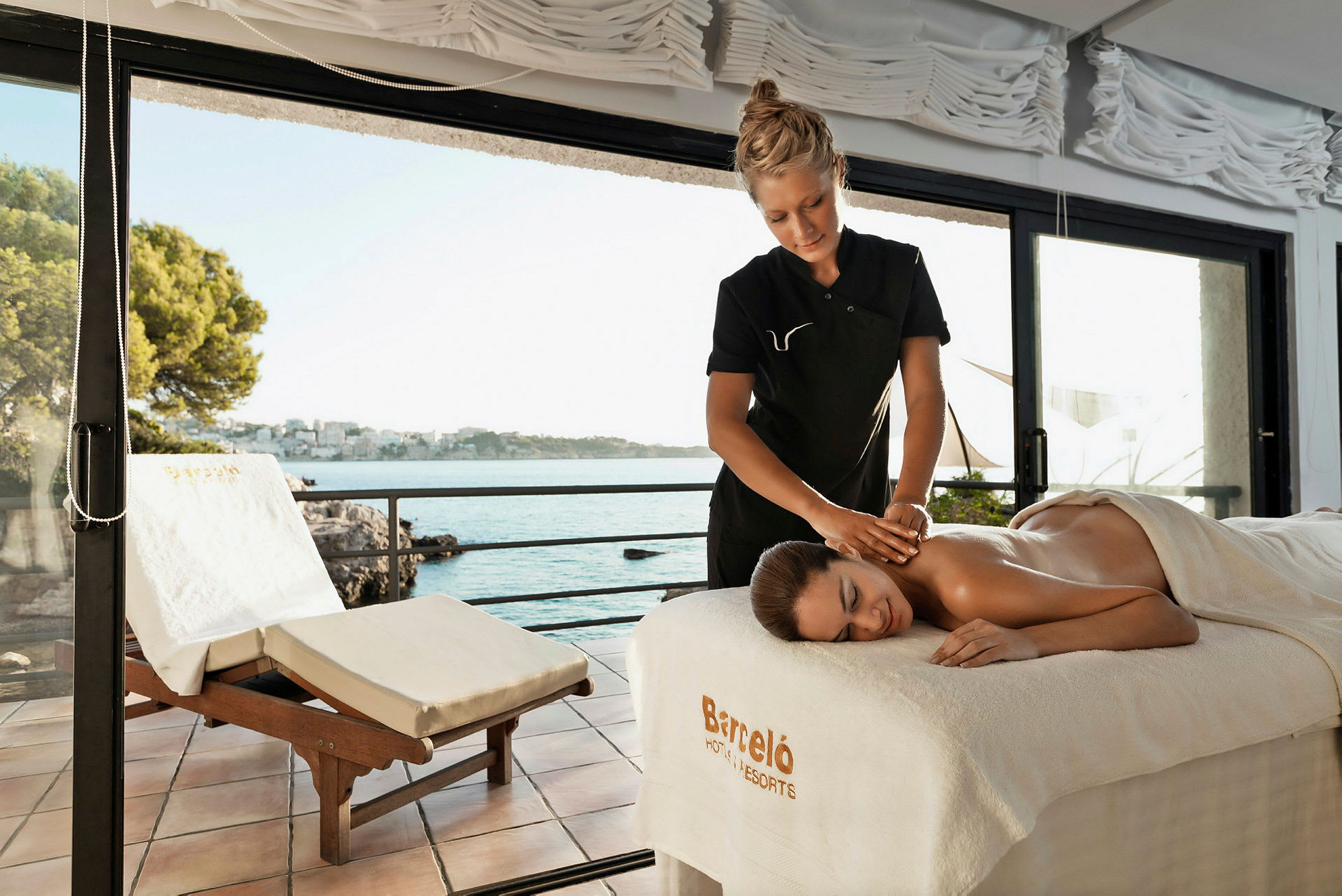 Massage utförs i en ljus miljö med utsikt över havet genom stora glasfönster. (AI-genererad text)