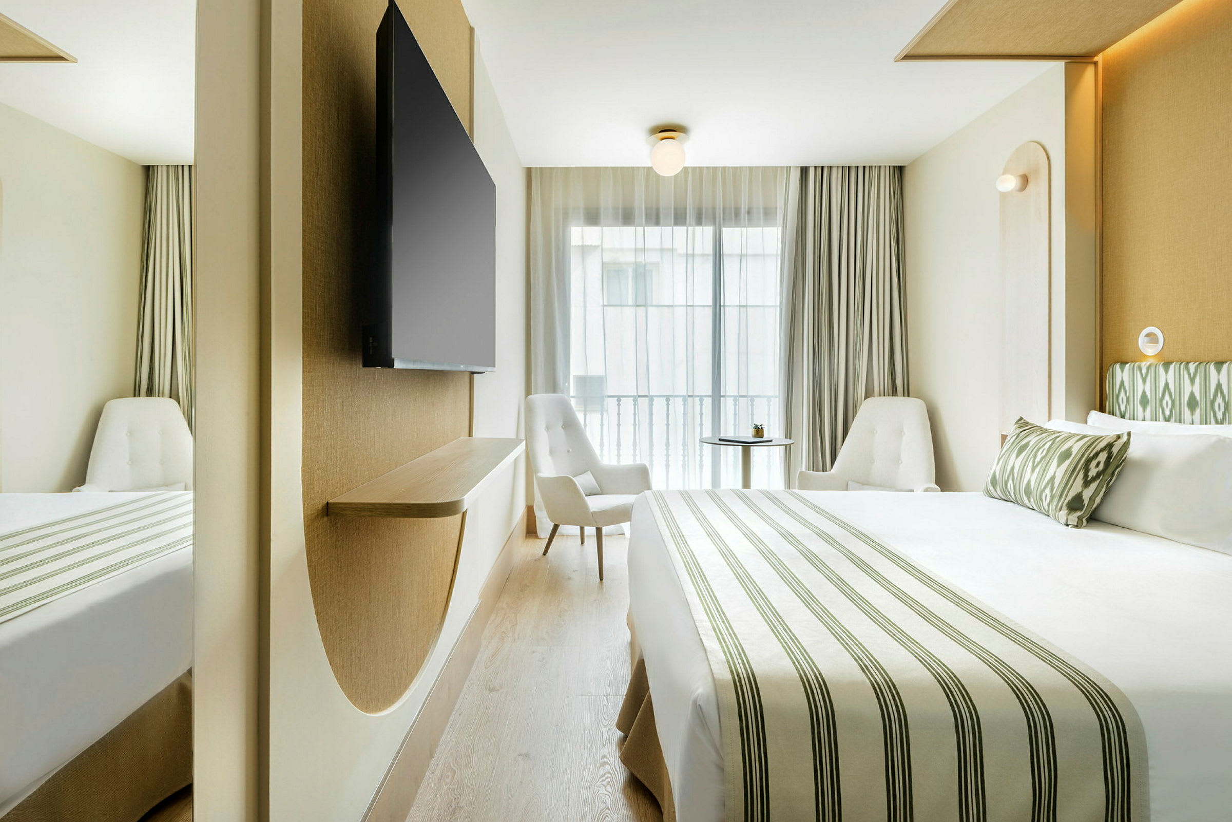Ett modernt hotellrum med en stor säng, två fåtöljer och en väggmonterad TV. (AI-genererad text)