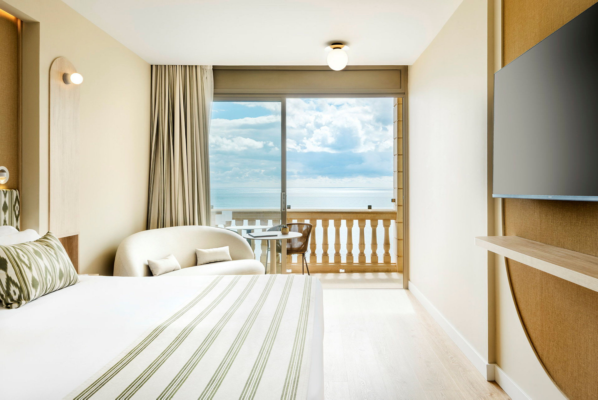 Ett hotellrum med havsutsikt från balkongen. Ett stort fönster vetter mot havet. (AI-genererad text)