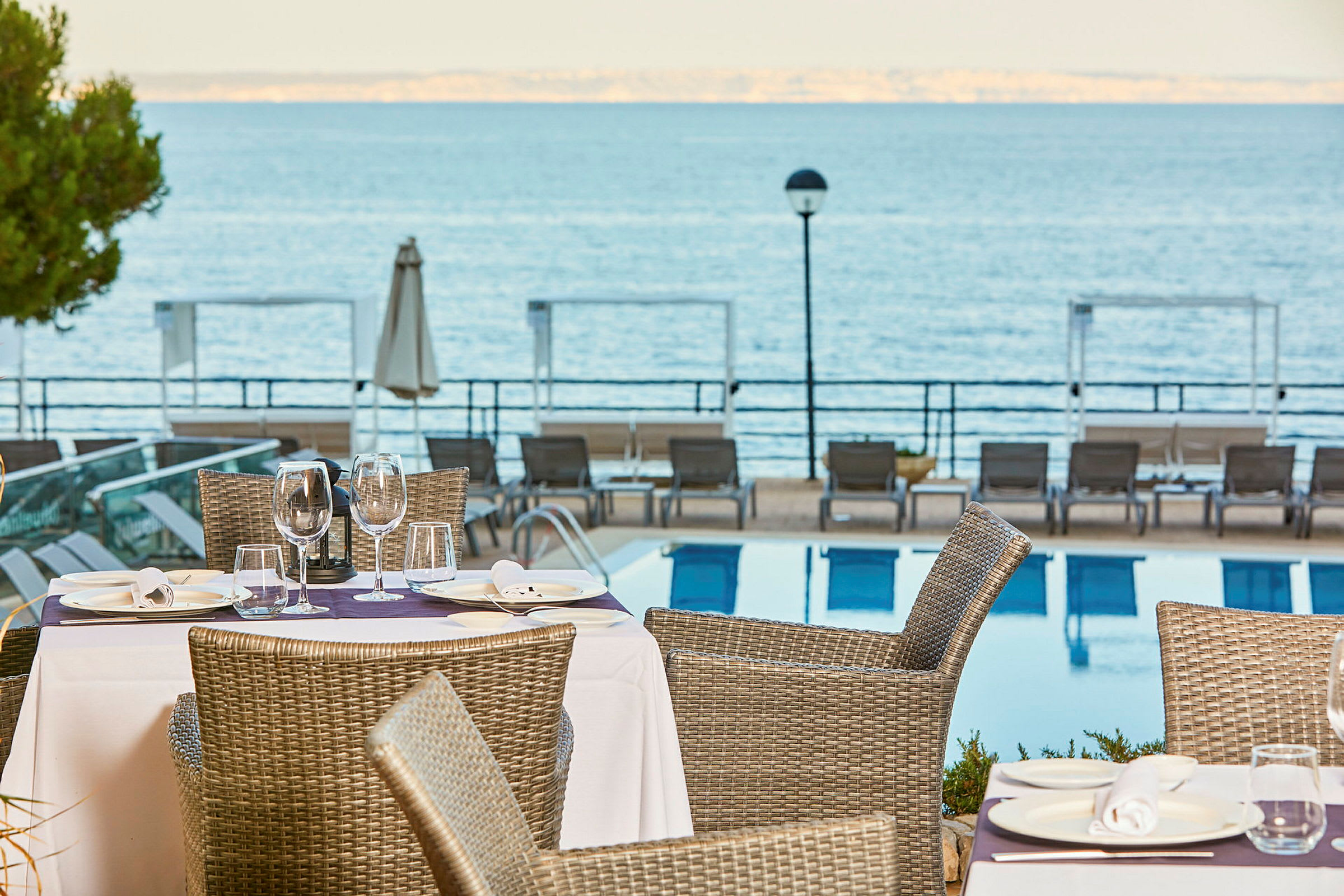 Uteservering med dukade bord vid en pool, med utsikt över havet. (AI-genererad text)