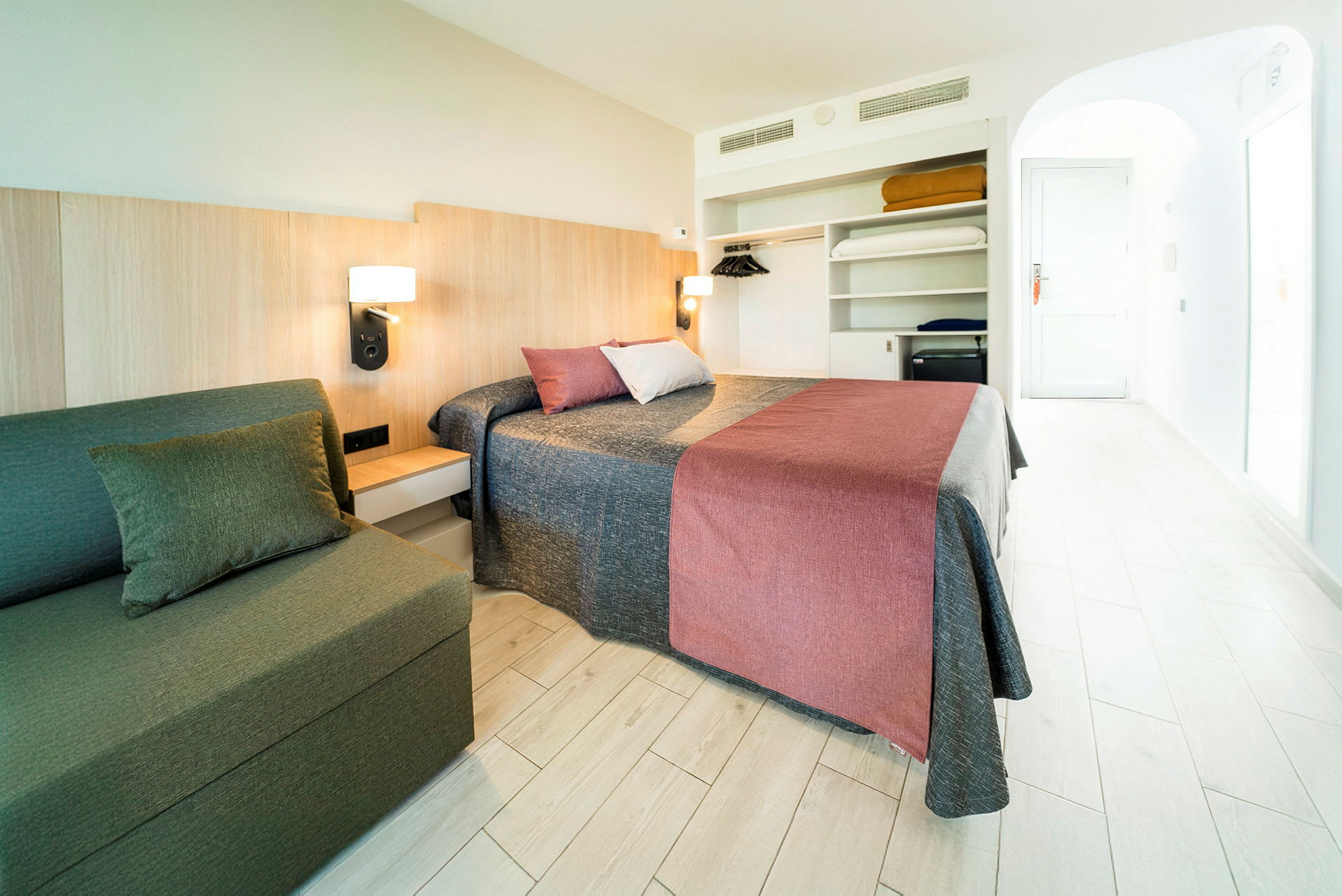 Ett hotellrum med en dubbelsäng, en soffa och en öppen garderob. (AI-genererad text)