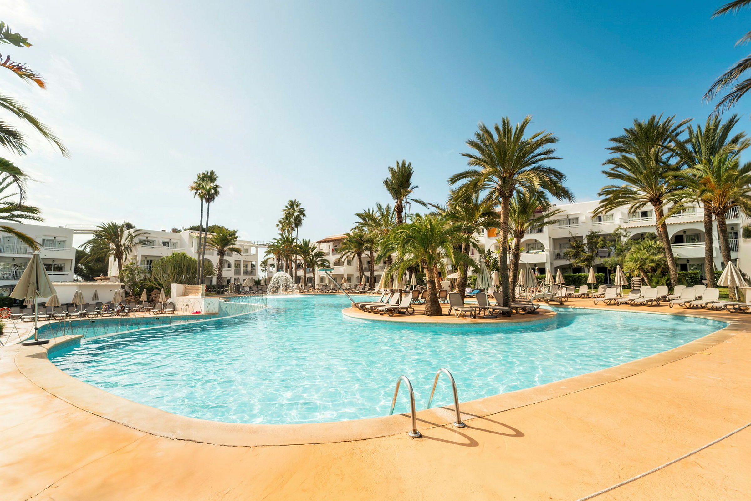 En pool omgiven av palmträd och solstolar på ett hotellområde. (AI-genererad text)
