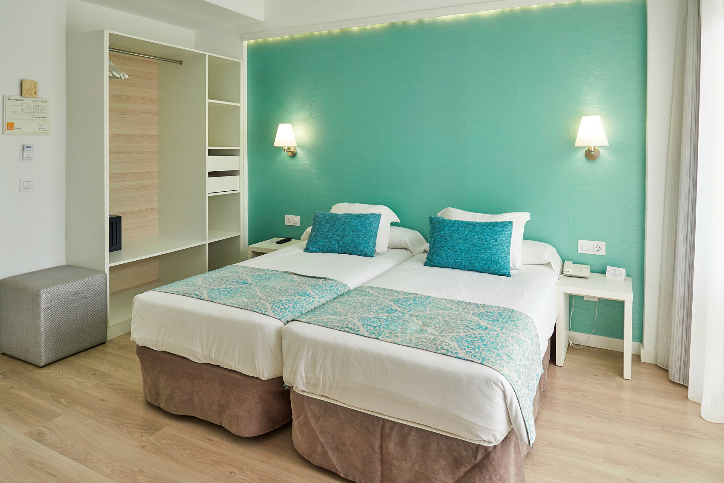 Ett hotellrum med två enkelsängar, turkosa kuddar och väggar. (AI-genererad text)