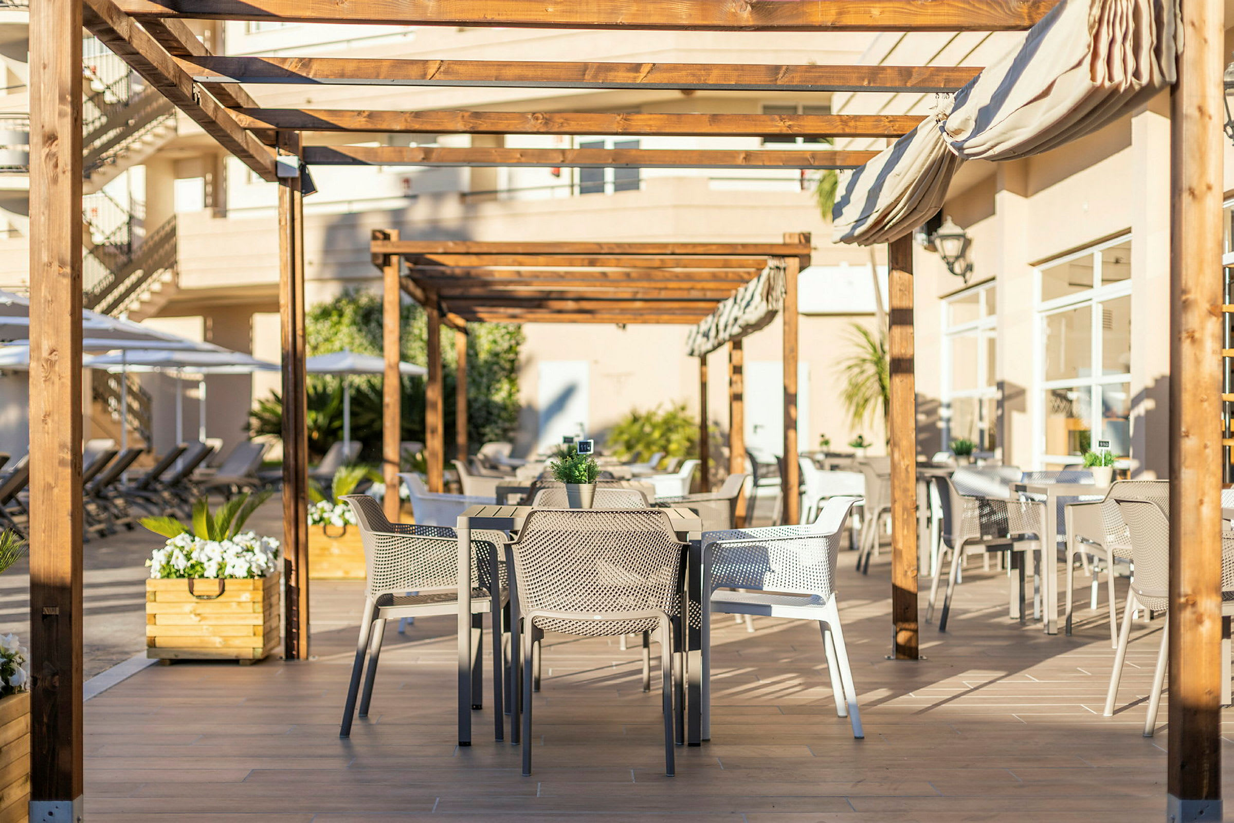 Uteservering under träpergola med bord och stolar. (AI-genererad text)