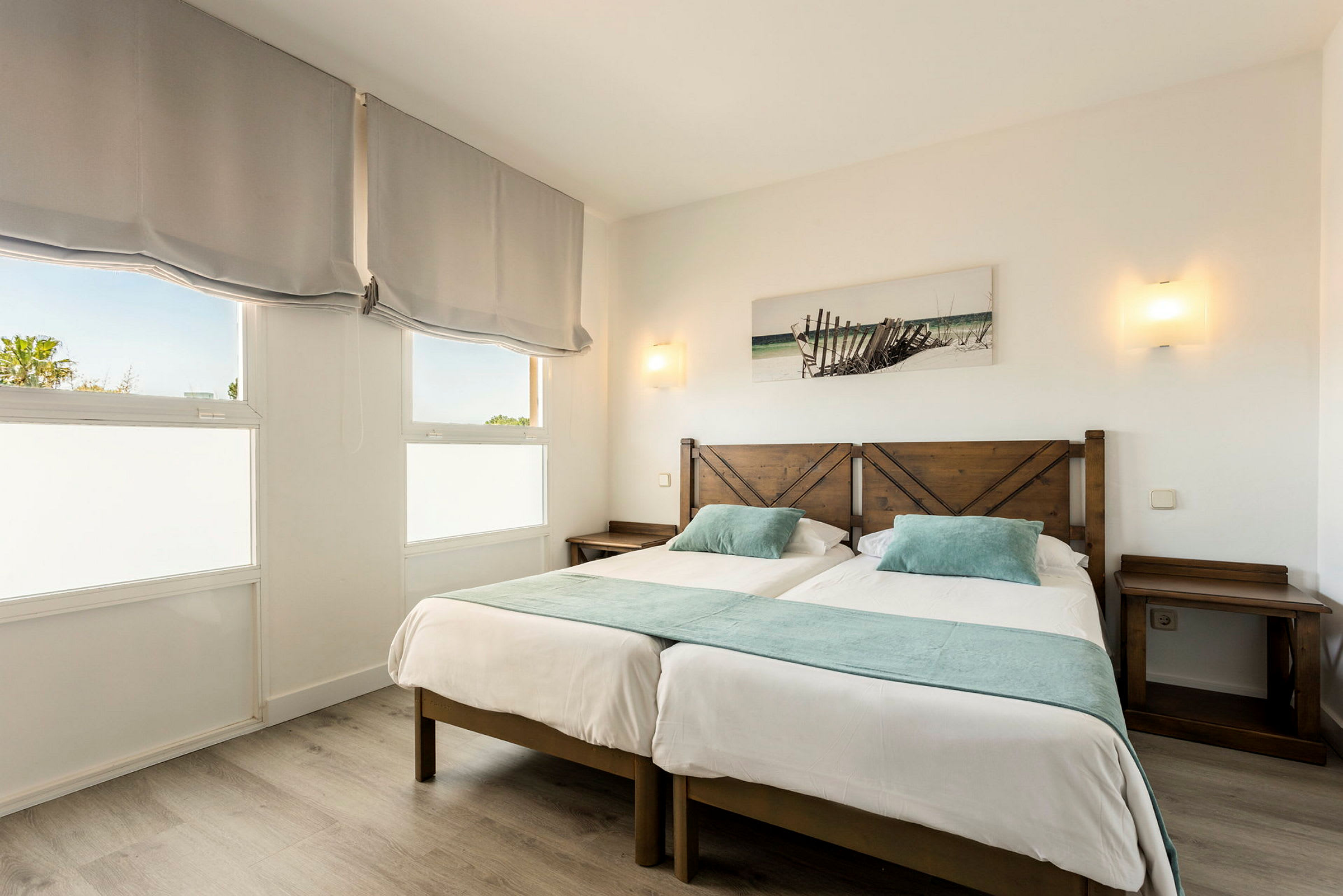 Bild på ett hotellrum med två enkelsängar, ljusa trädetaljer och dekorativa element. (AI-genererad text)