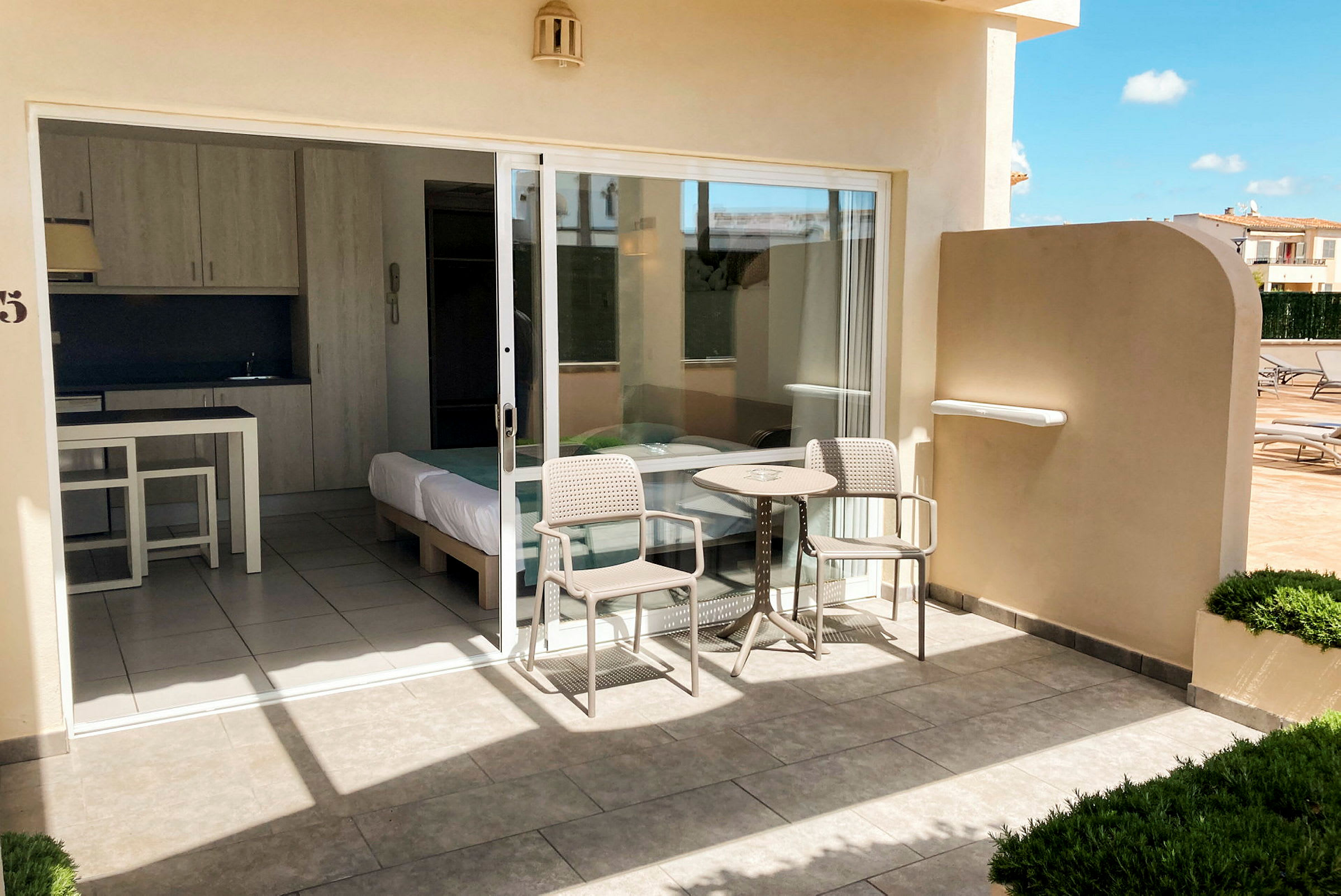 Uteplats med bord och stolar framför ett hotellrum med glasdörr. (AI-genererad text)