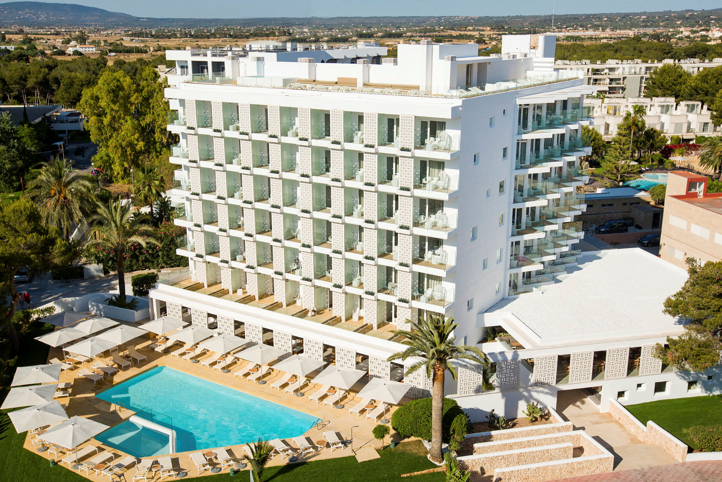 En modern hotellbyggnad med en pool och solstolar runt den, omgiven av träd och grönska. (AI-genererad text)