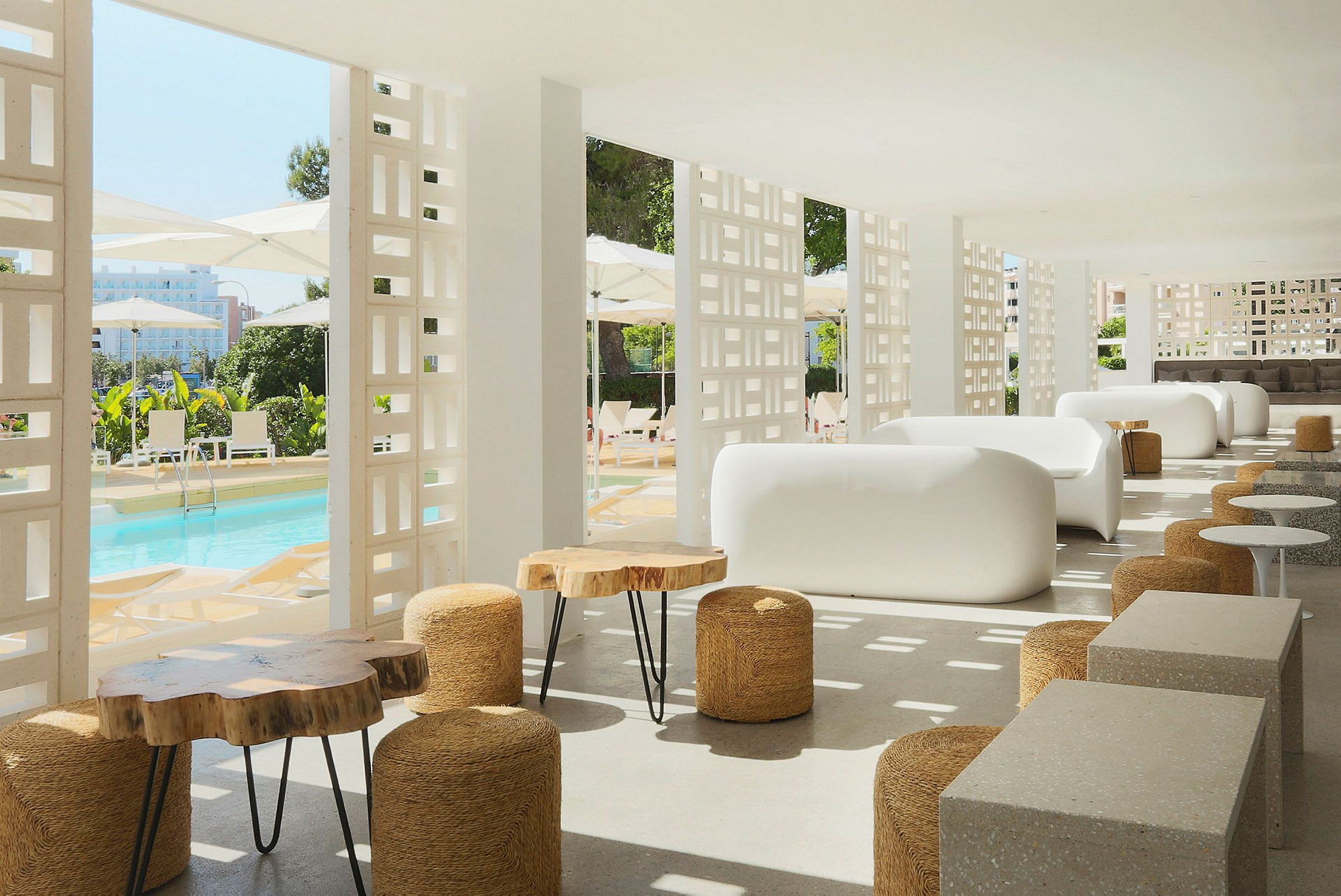 Modern lounge inredd med vita soffor och träbord, med utsikt över en pool och parasoller. (AI-genererad text)