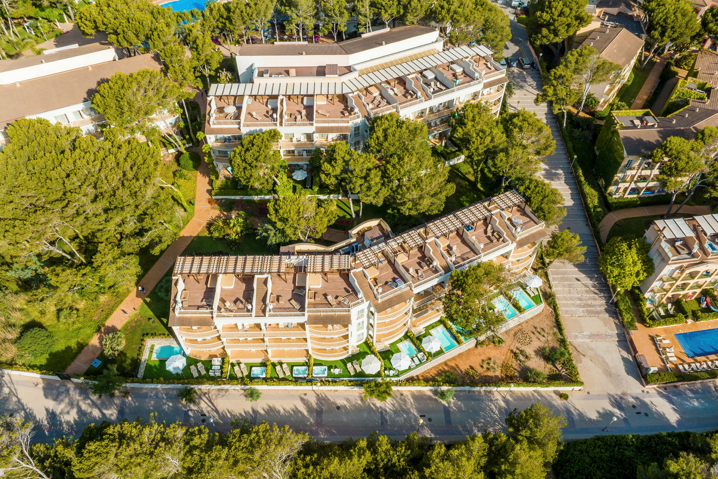 Flygfoto av hotellbyggnader omgivna av grönska och poolområden. (AI-genererad text)