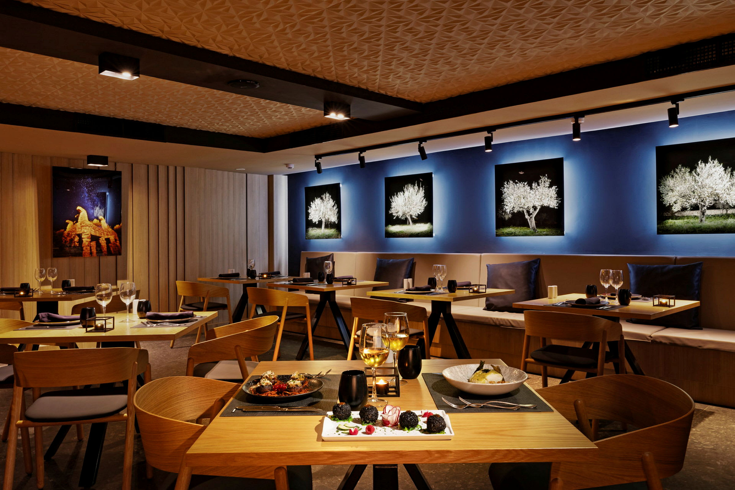 Interiör av en restaurang med träbord och stolar, dekorativa väggbilder och serverad mat på borden. (AI-genererad text)
