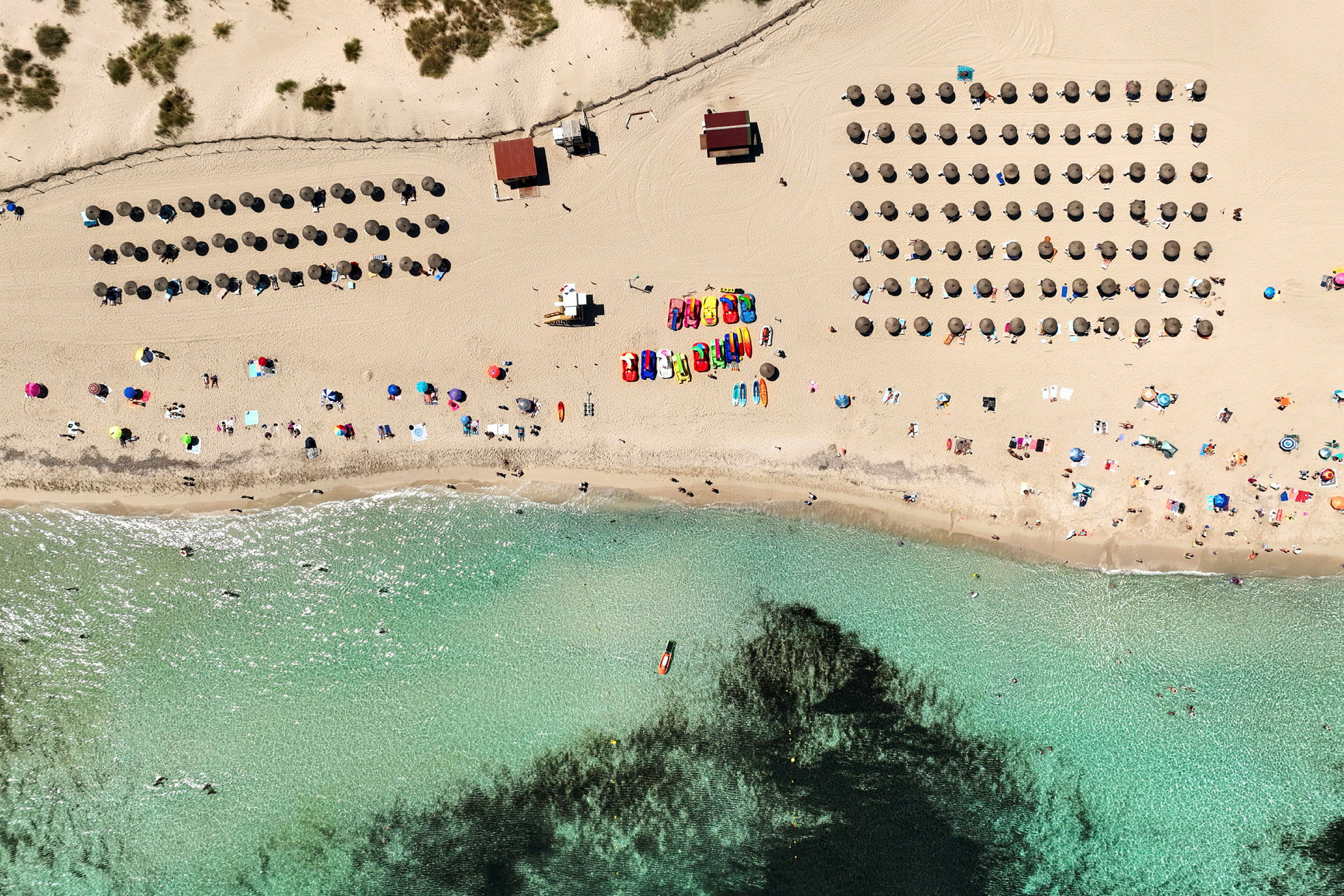 Luftvy över en strand med parasoller, människor och klart vatten. (AI-genererad text)