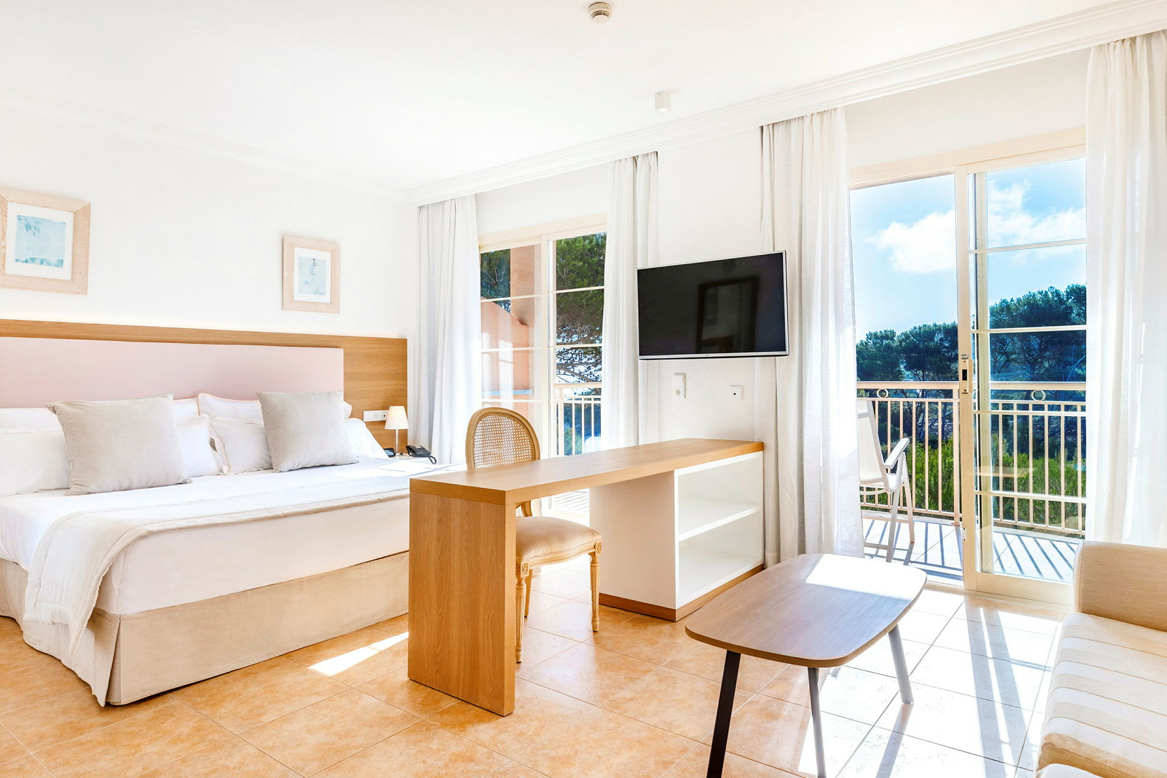 Ett ljust hotellrum med dubbelsäng, skrivbord, fåtölj och balkong med utsikt. (AI-genererad text)