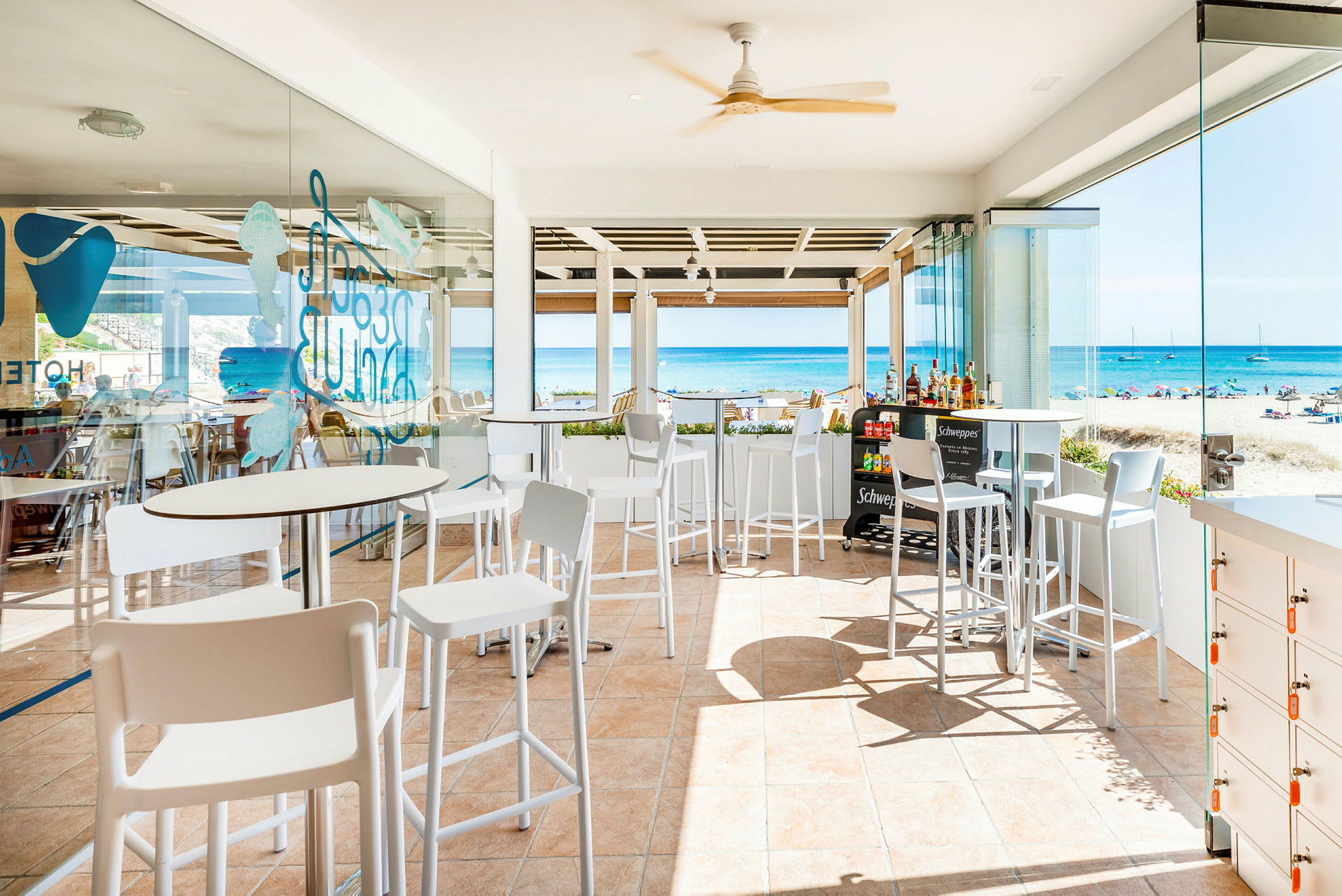 En ljus restaurang med vita möbler, havsutsikt och glasväggar. (AI-genererad text)