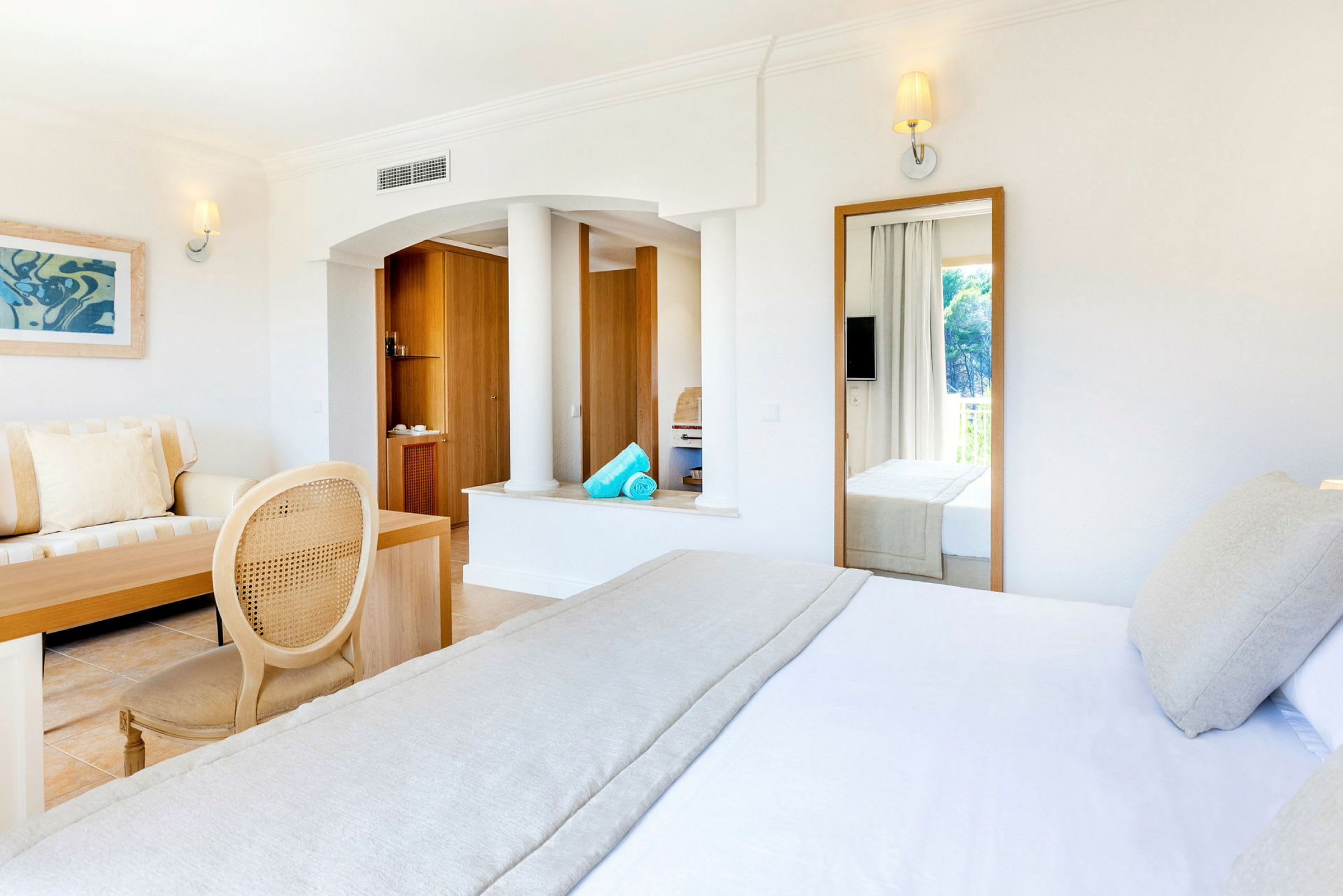Ljust hotellrum med säng, soffa, och stora speglar. (AI-genererad text)