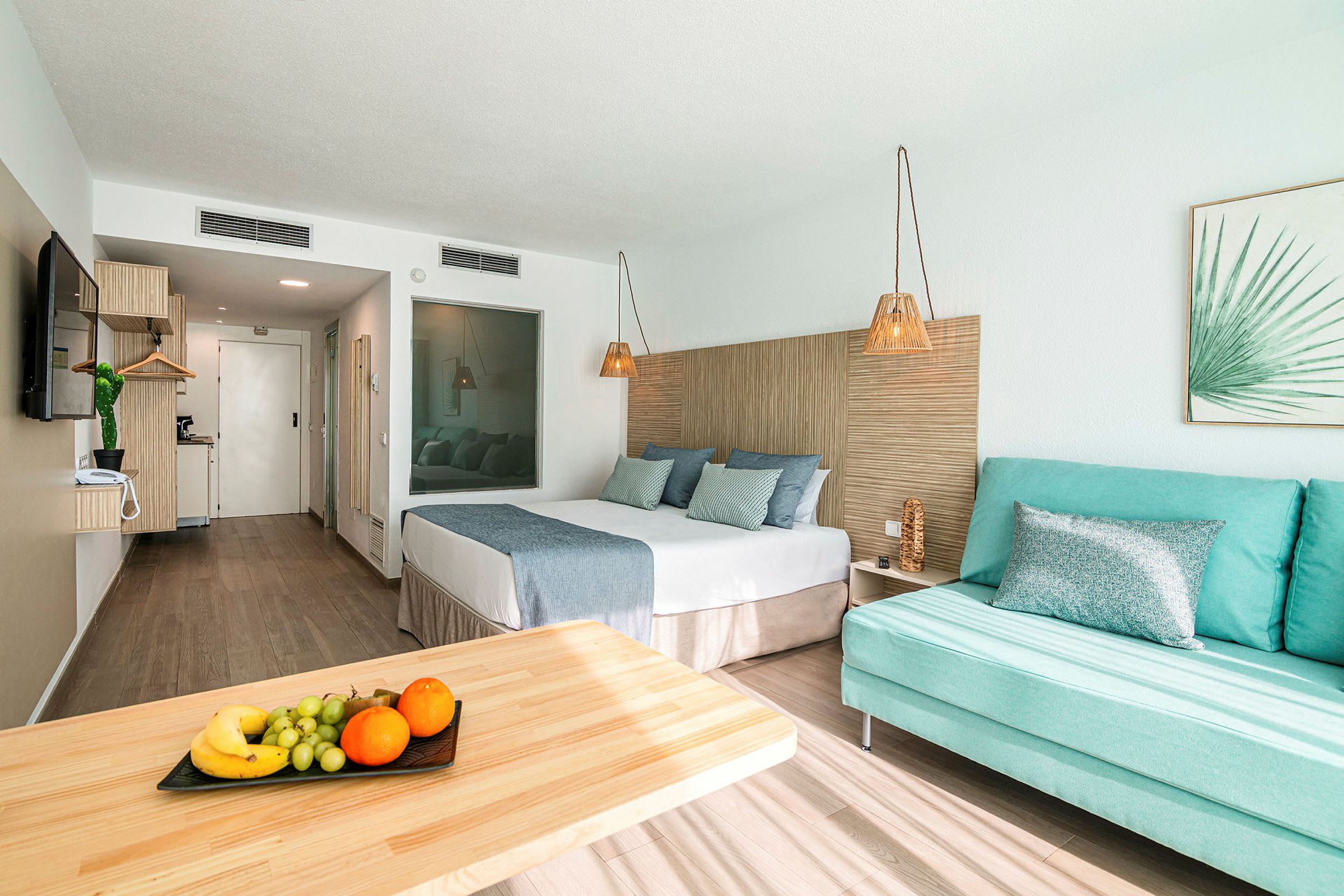 Hotellrum med säng, soffa och bord med frukt. (AI-genererad text)