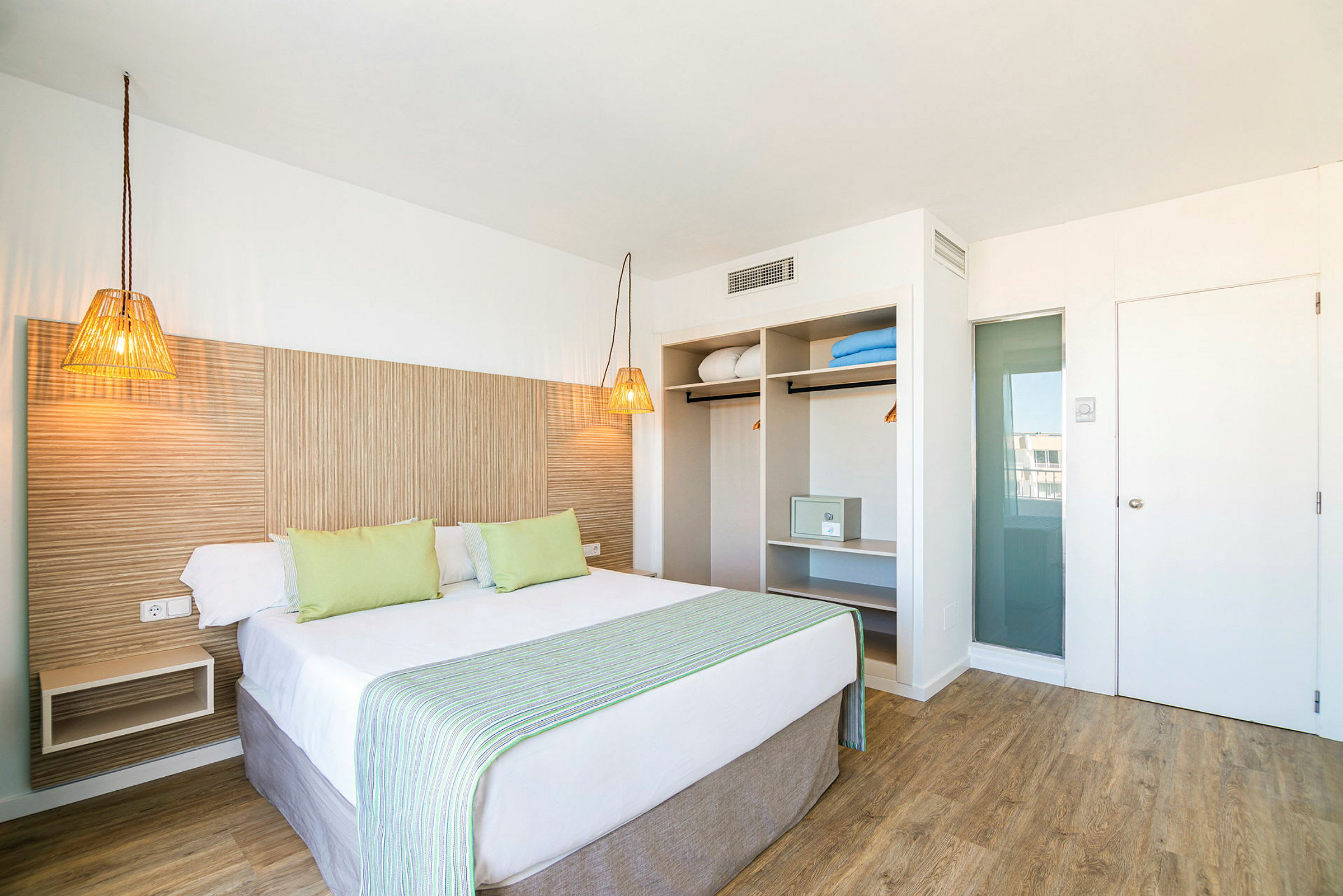 Ett hotellrum med en dubbelsäng, ljusa möbler och öppen garderob. (AI-genererad text)