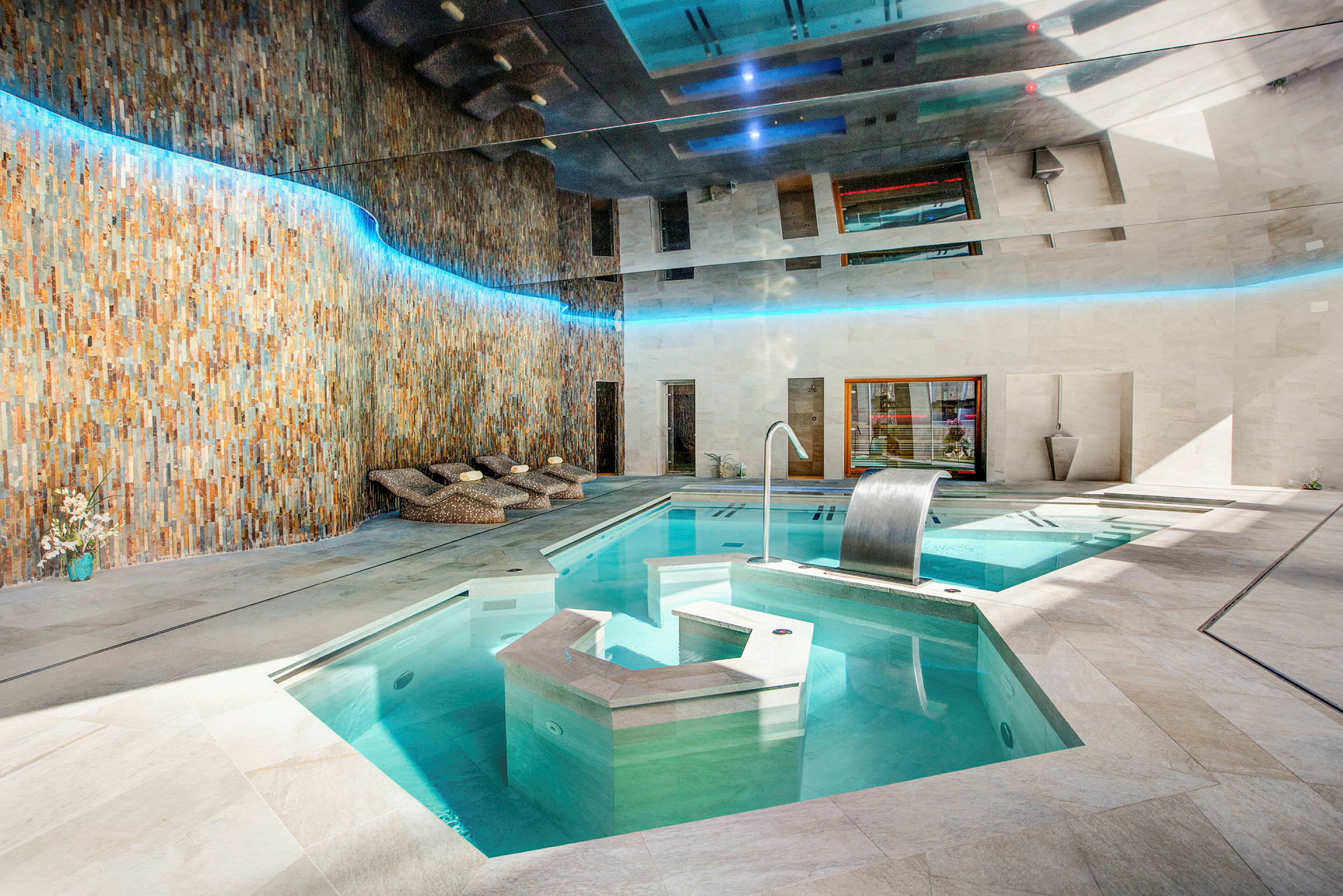 Inomhuspool med vattenfall och solstolar. (AI-genererad text)