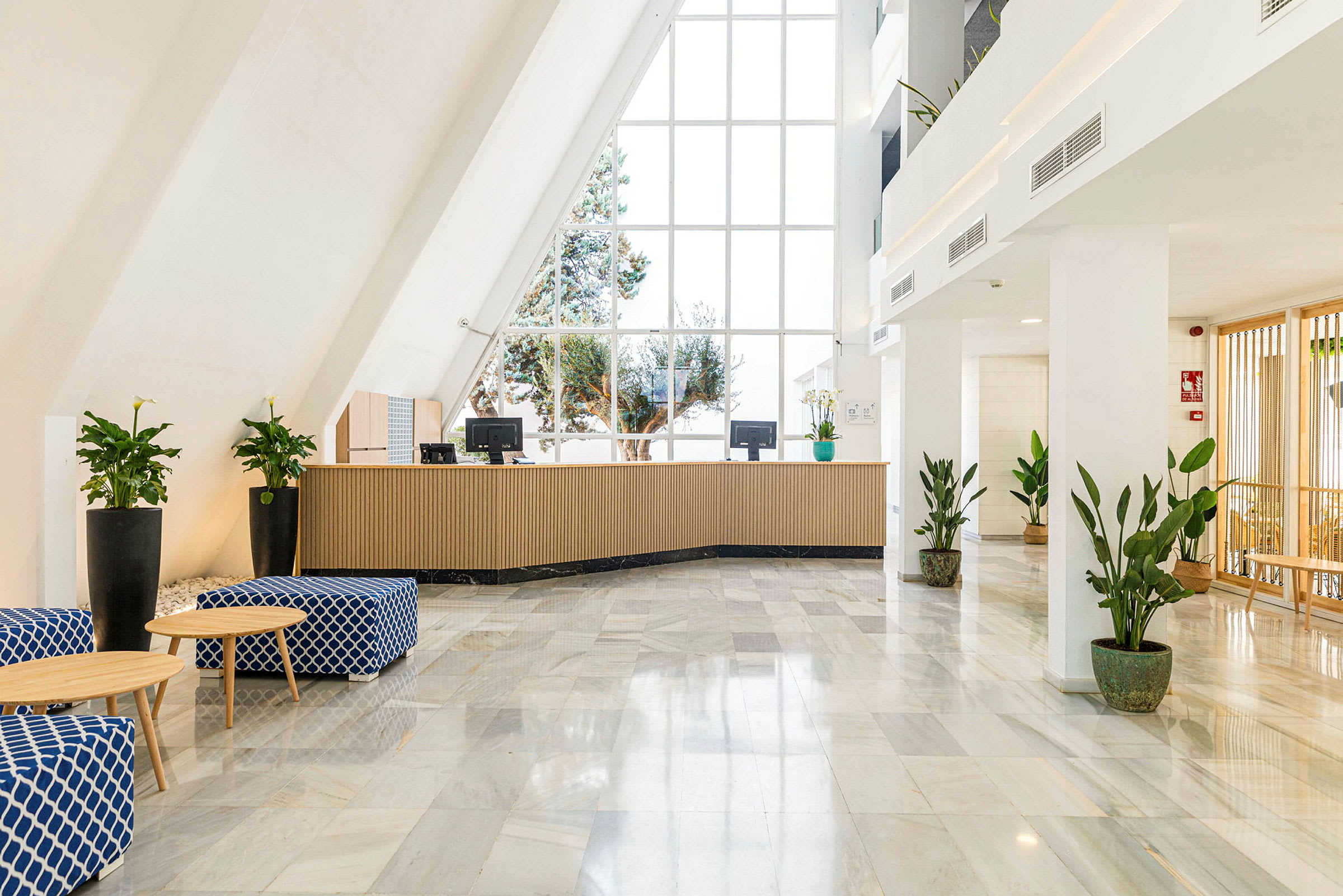 Hotellreception med stora fönster, soffstolar och krukväxter. (AI-genererad text)