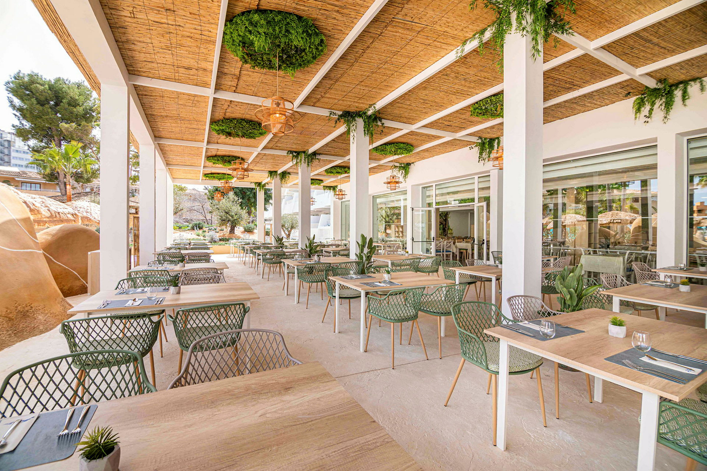 Utomhusrestaurang med bord och stolar under ett tak med gröna växter. (AI-genererad text)