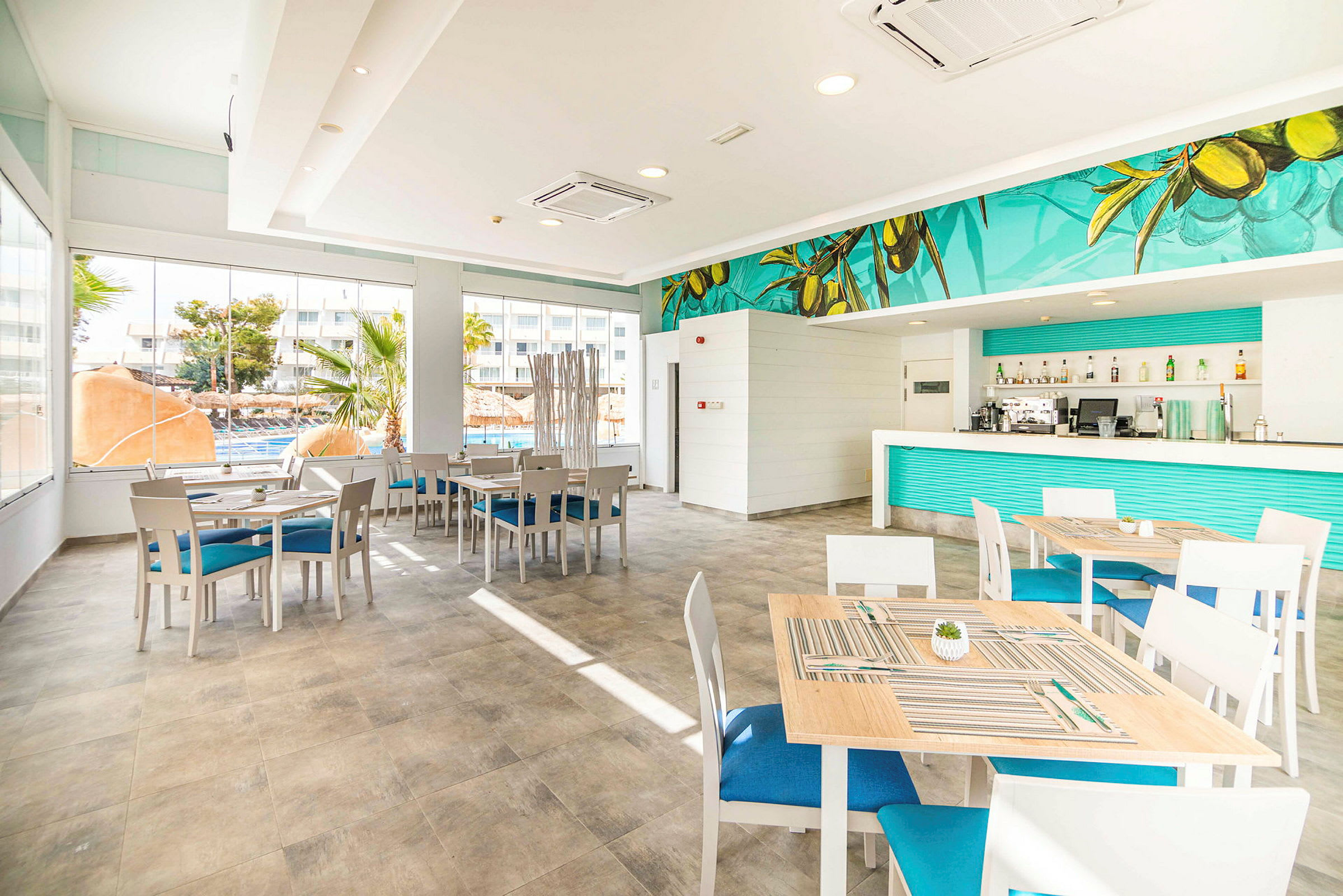 Ljusa möbler i en modern restaurang med blå detaljer och stora fönster. (AI-genererad text)