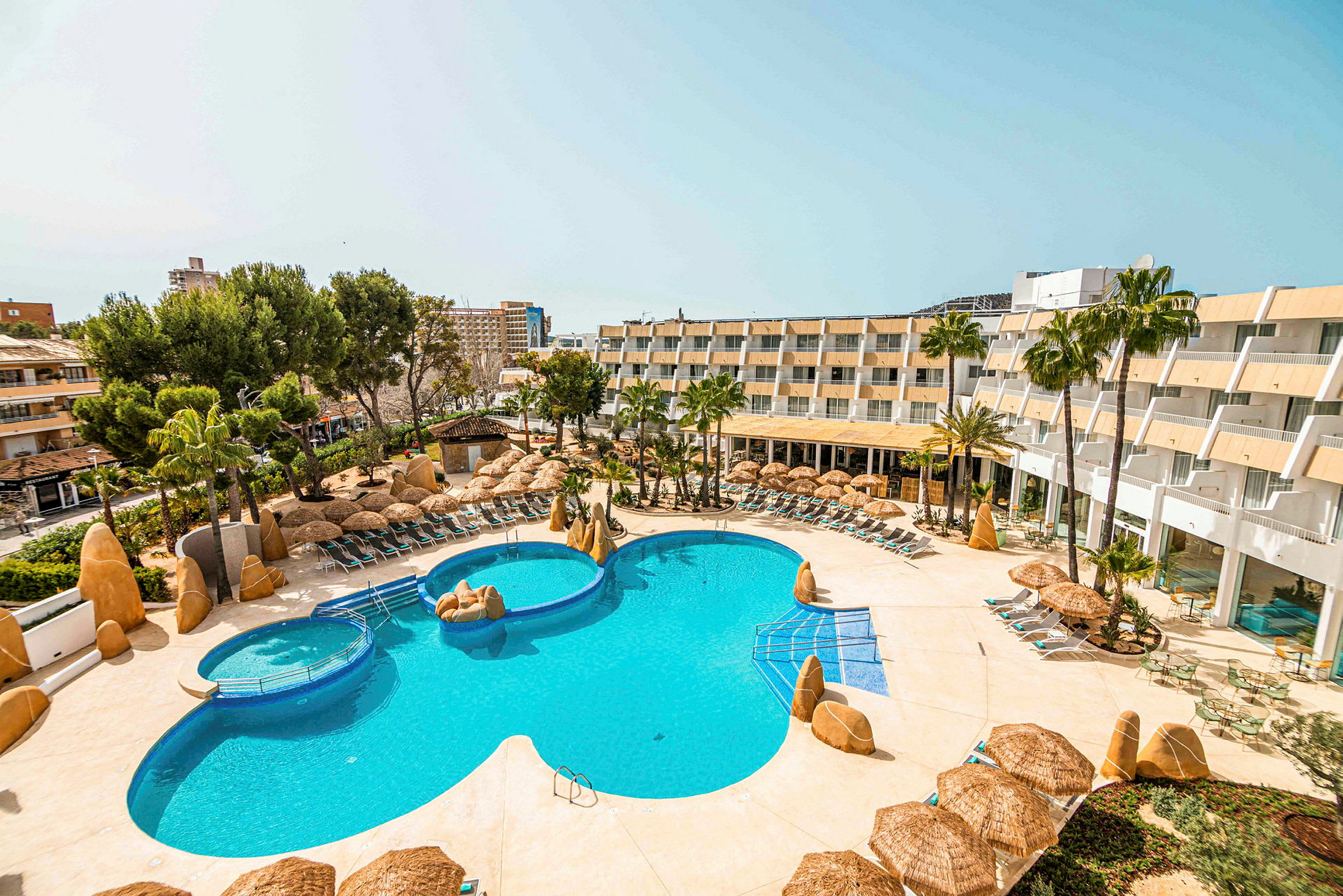 Bild av ett hotellområde med en stor pool omgiven av solstolar, parasoll och gröna palmer. (AI-genererad text)