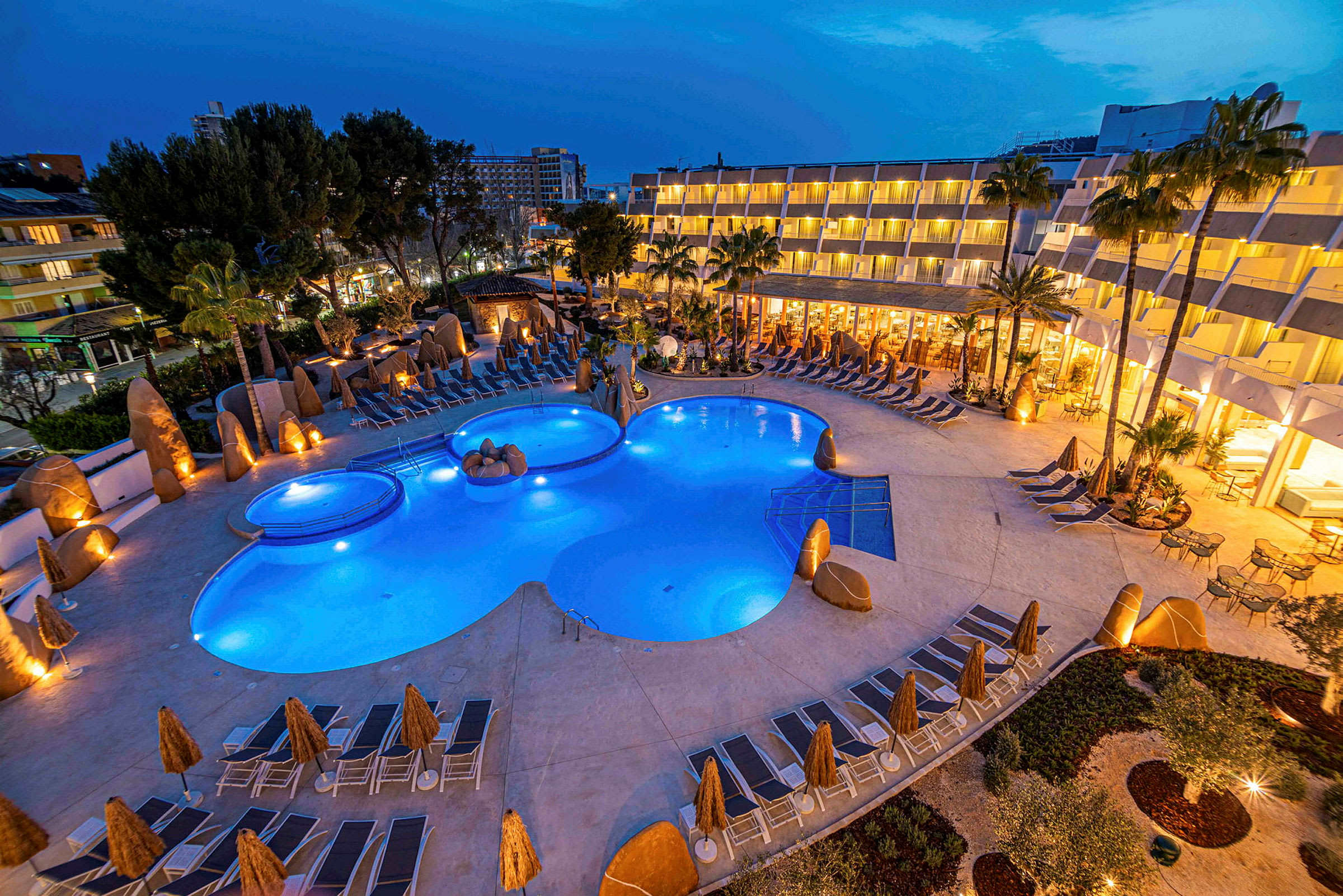 Upplyst hotellområde med pool och solstolar på kvällen. (AI-genererad text)