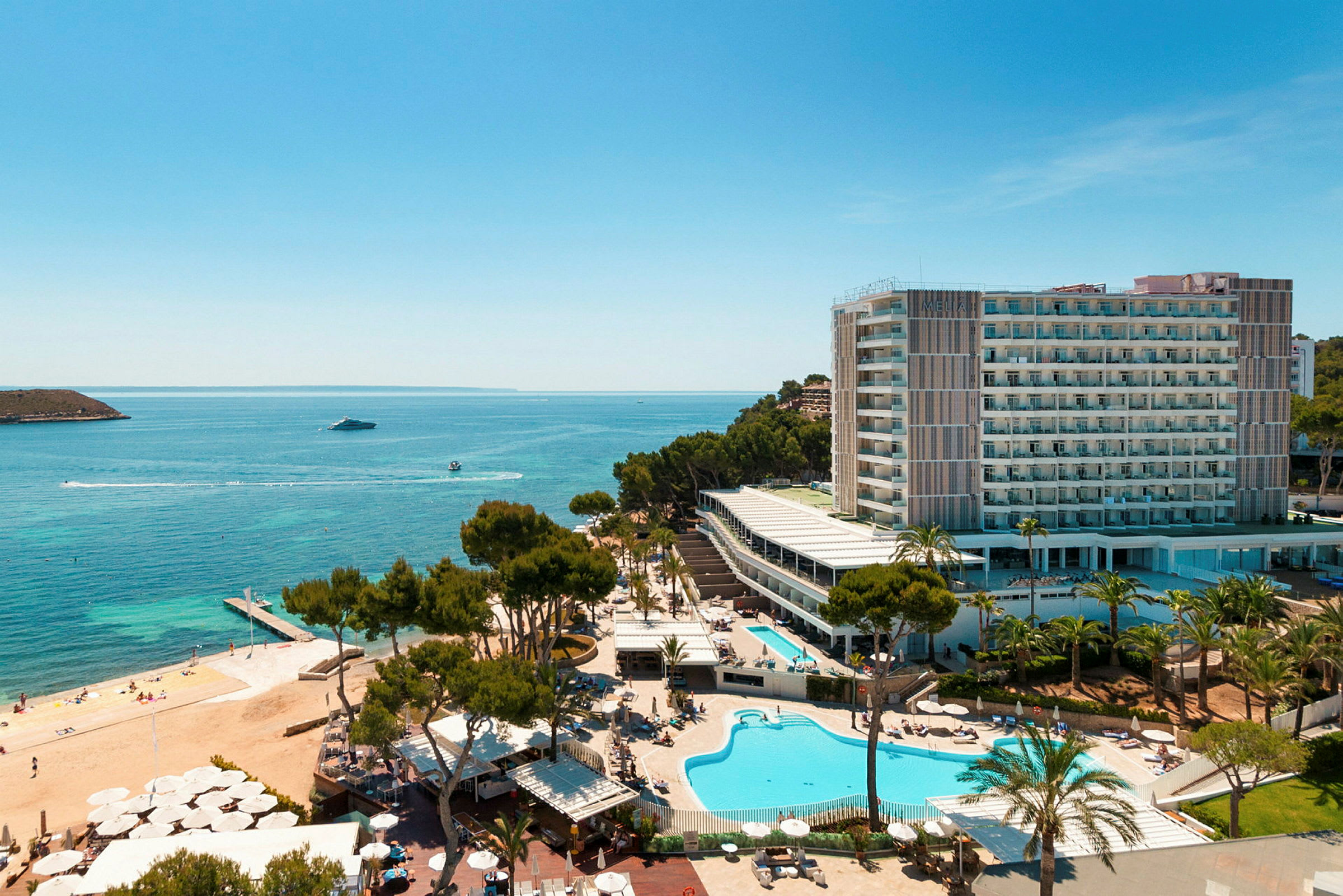Flygfoto av ett hotellkomplex vid havet med pooler, grönska och en strand. (AI-genererad text)