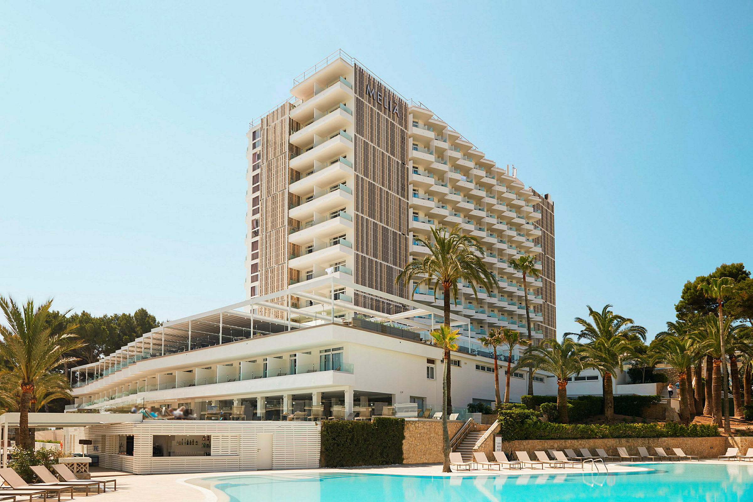 Ett höghushotell med modern arkitektur beläget bredvid en utomhuspool och omgiven av palmer. (AI-genererad text)