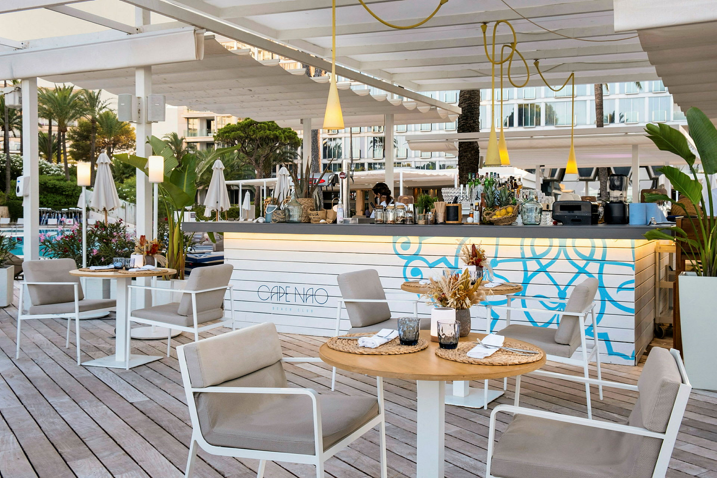 Utomhusmiljö vid en strandklubb med sittgrupper, ett dekorativt barområde och gröna plantor. (AI-genererad text)