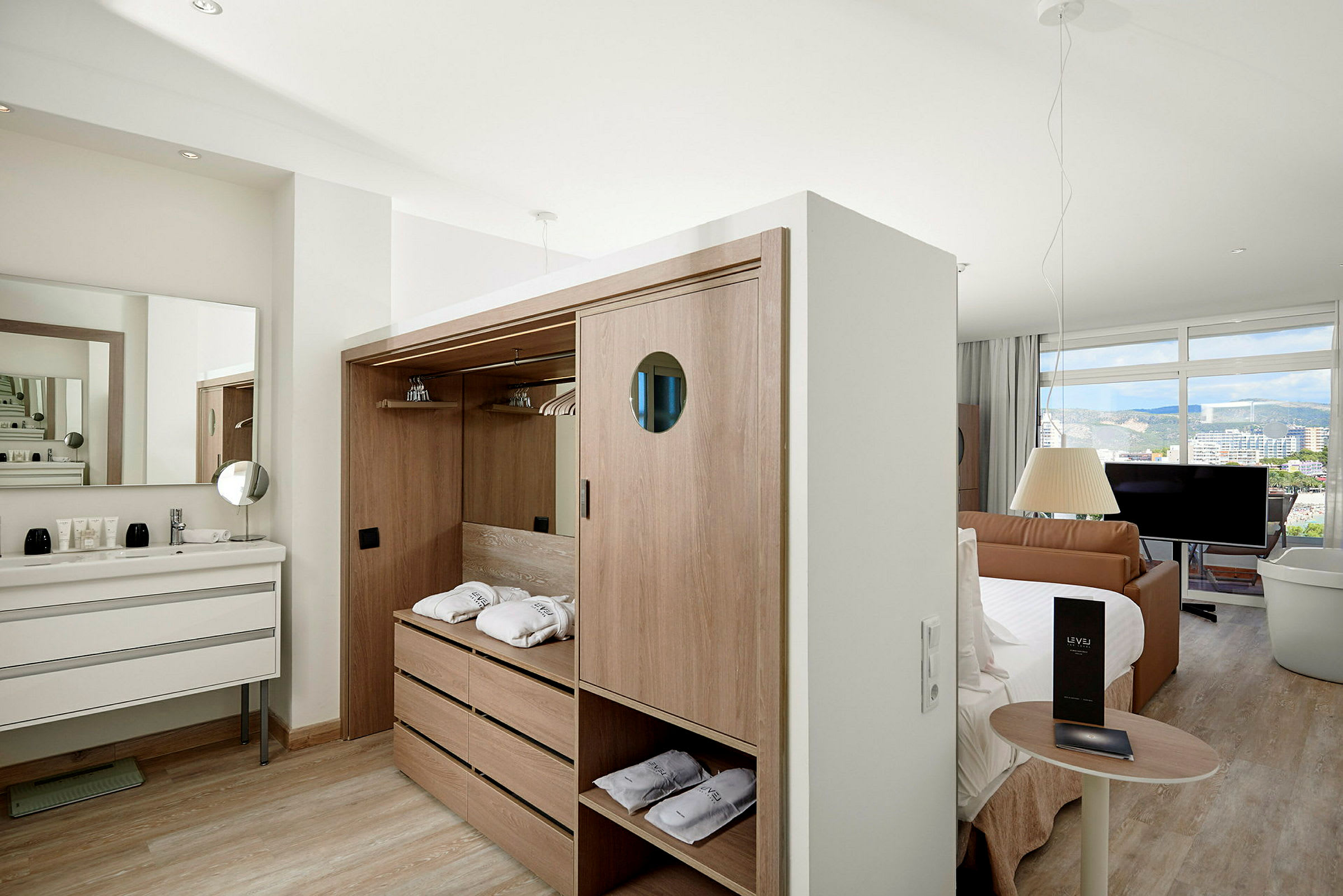 Ett hotellrum med garderob, handfat, säng, soffa och en stor fönstervy. (AI-genererad text)