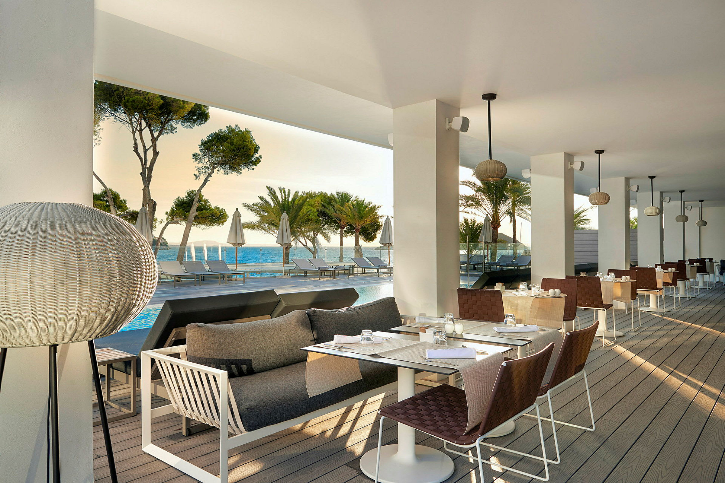 Restaurang med sittplatser på en terrass med utsikt över havet och omgivande palmer. (AI-genererad text)