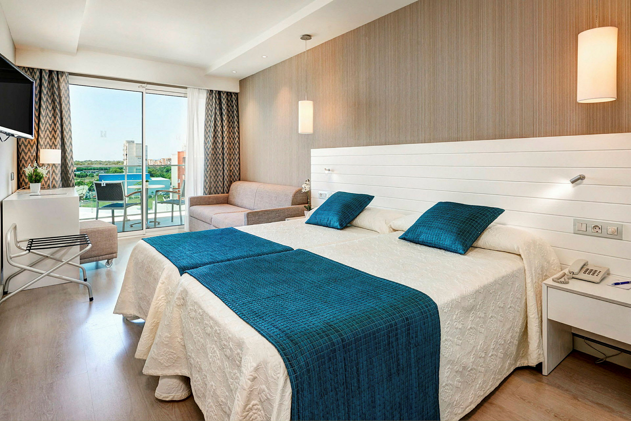 Hotellrum med två sängar, en soffa och en glasbalkong. (AI-genererad text)