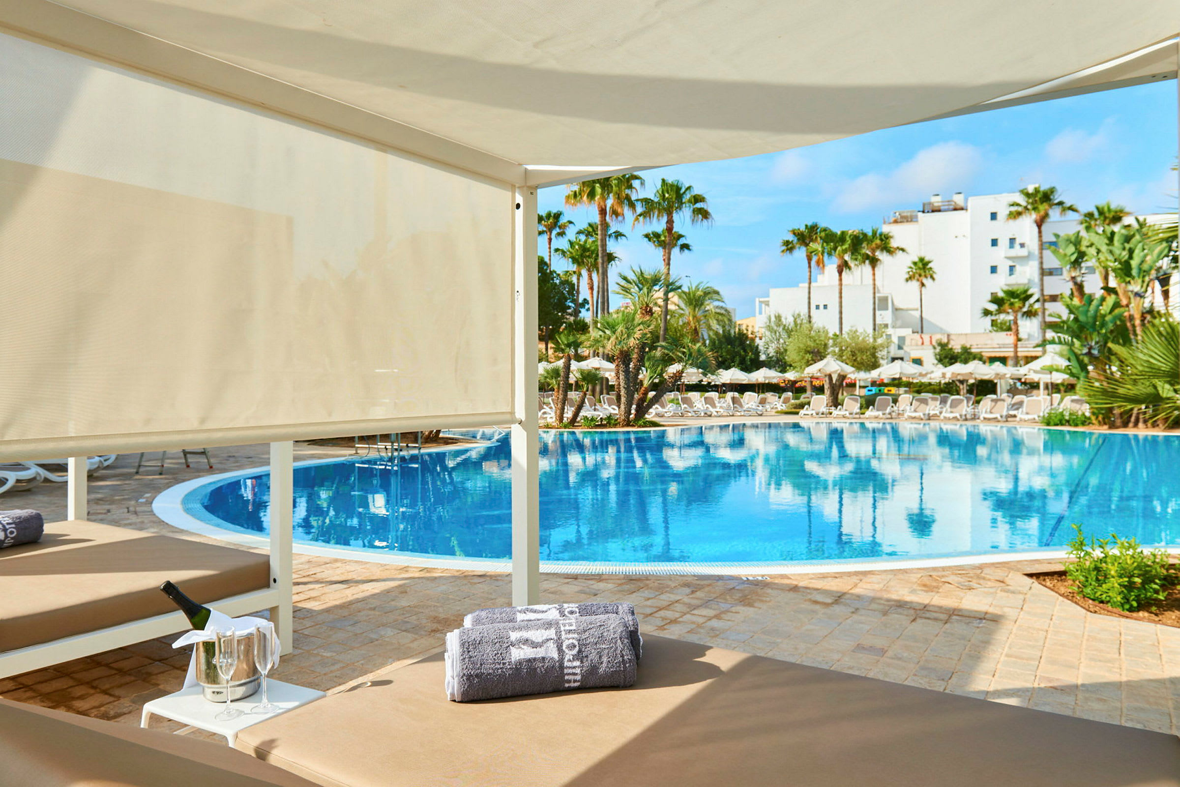 En lyxig cabana nära en pool med palmer och parasoller runt omkring. (AI-genererad text)