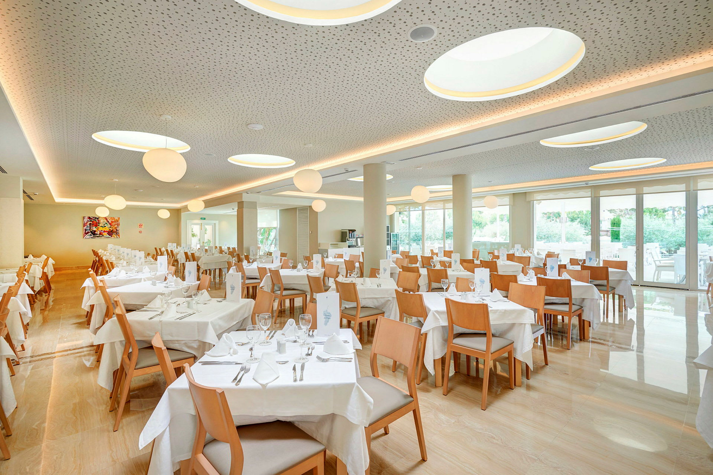En restaurang med flera dukade bord och trästolar, stora fönster och taklampor. (AI-genererad text)