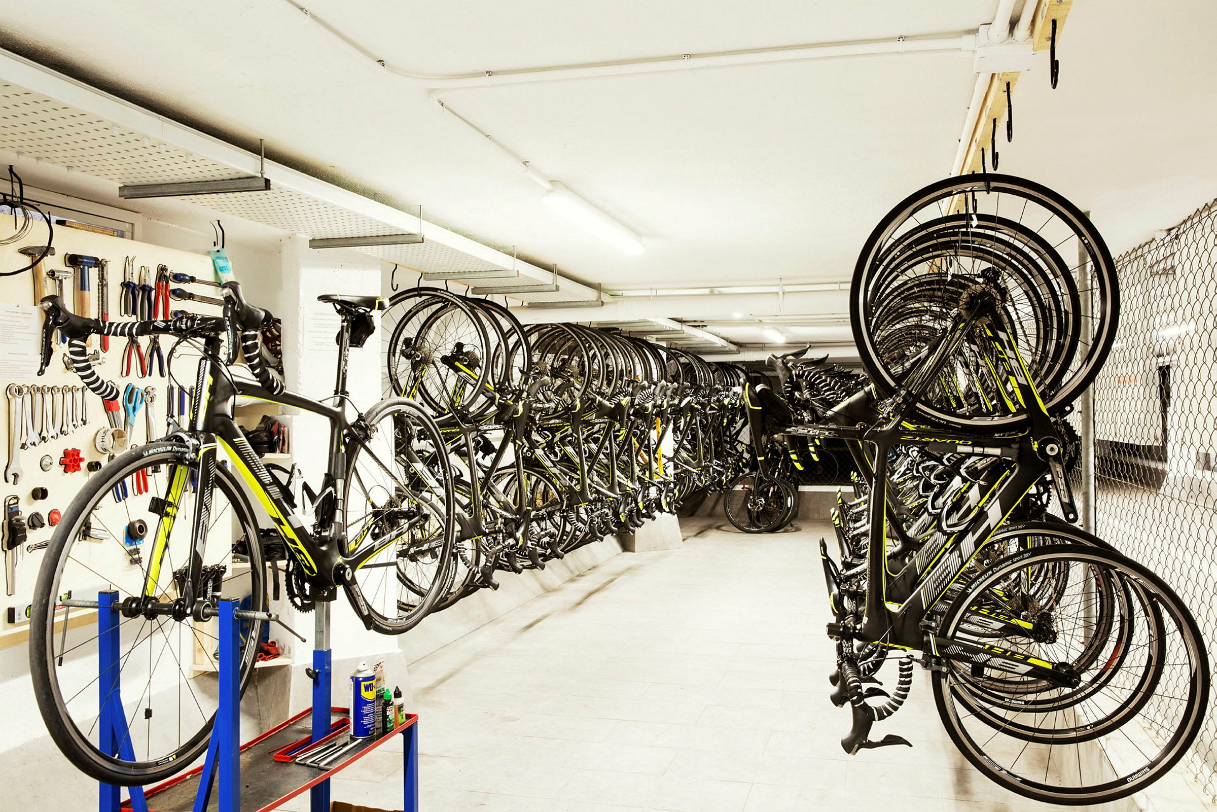 Cykelförråd med verktygstavla, cykel på monteringsställ och många landsvägscyklar hängande. (AI-genererad text)