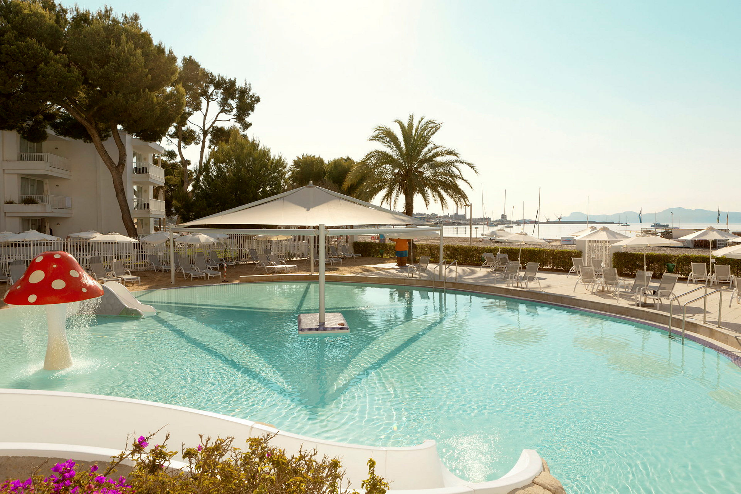 Pool med rutschkanor och parasoll vid havet. (AI-genererad text)