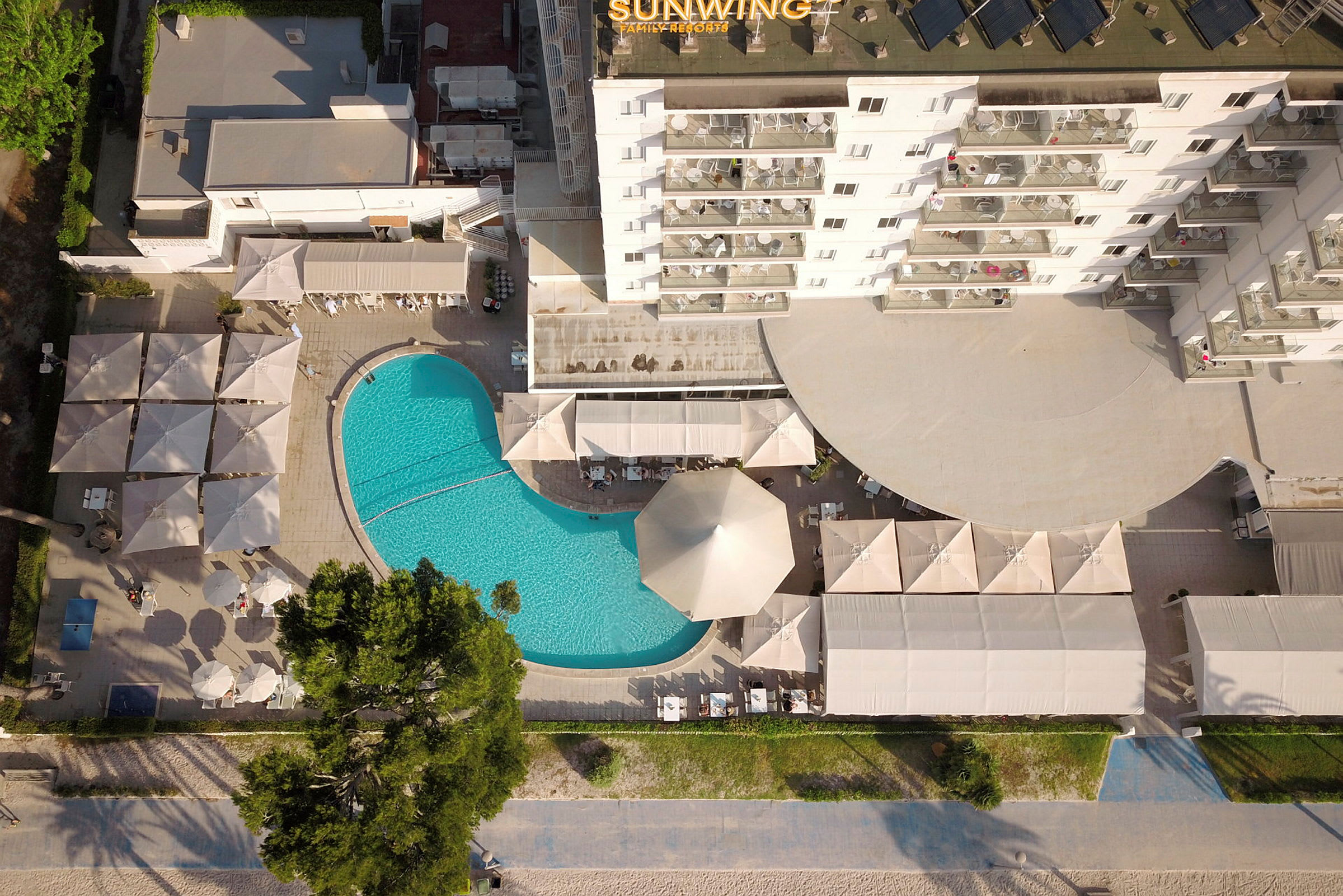 Flygbild av hotellområde med pool, parasoller och byggnader. (AI-genererad text)