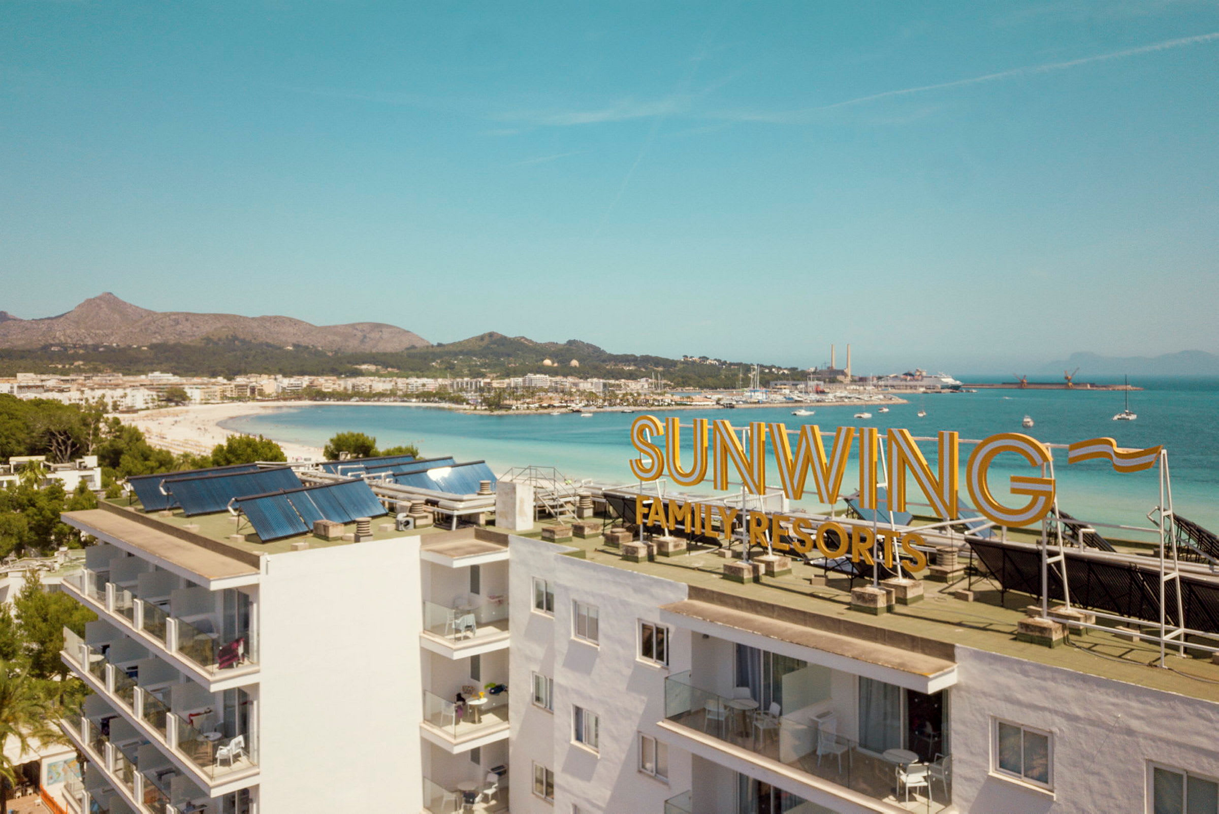 Bild med vy över stranden och havet, med texten 'Sunwing Family Resorts' på byggnadens tak. (AI-genererad text)