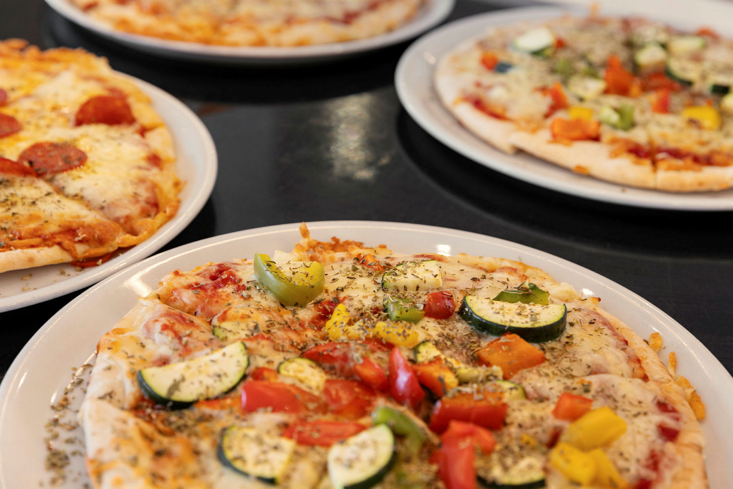 Fyra pizzor med olika tillbehör på tallrikar. (AI-genererad text)
