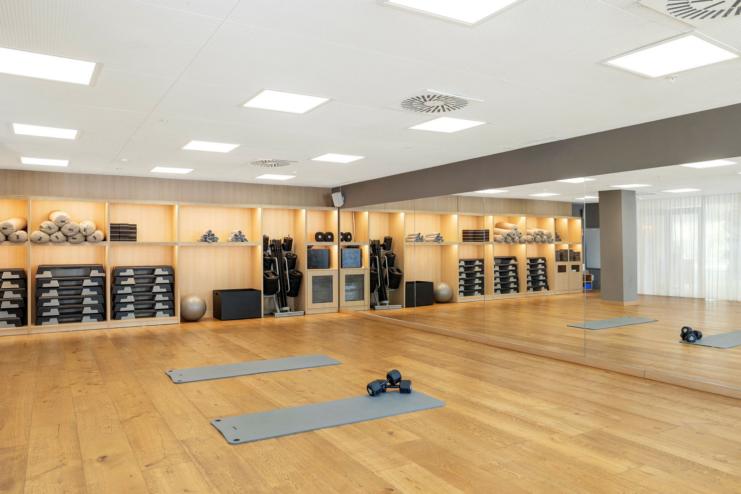 Ett gym med trägolv, spegelvägg och hyllor fyllda med träningsutrustning. (AI-genererad text)