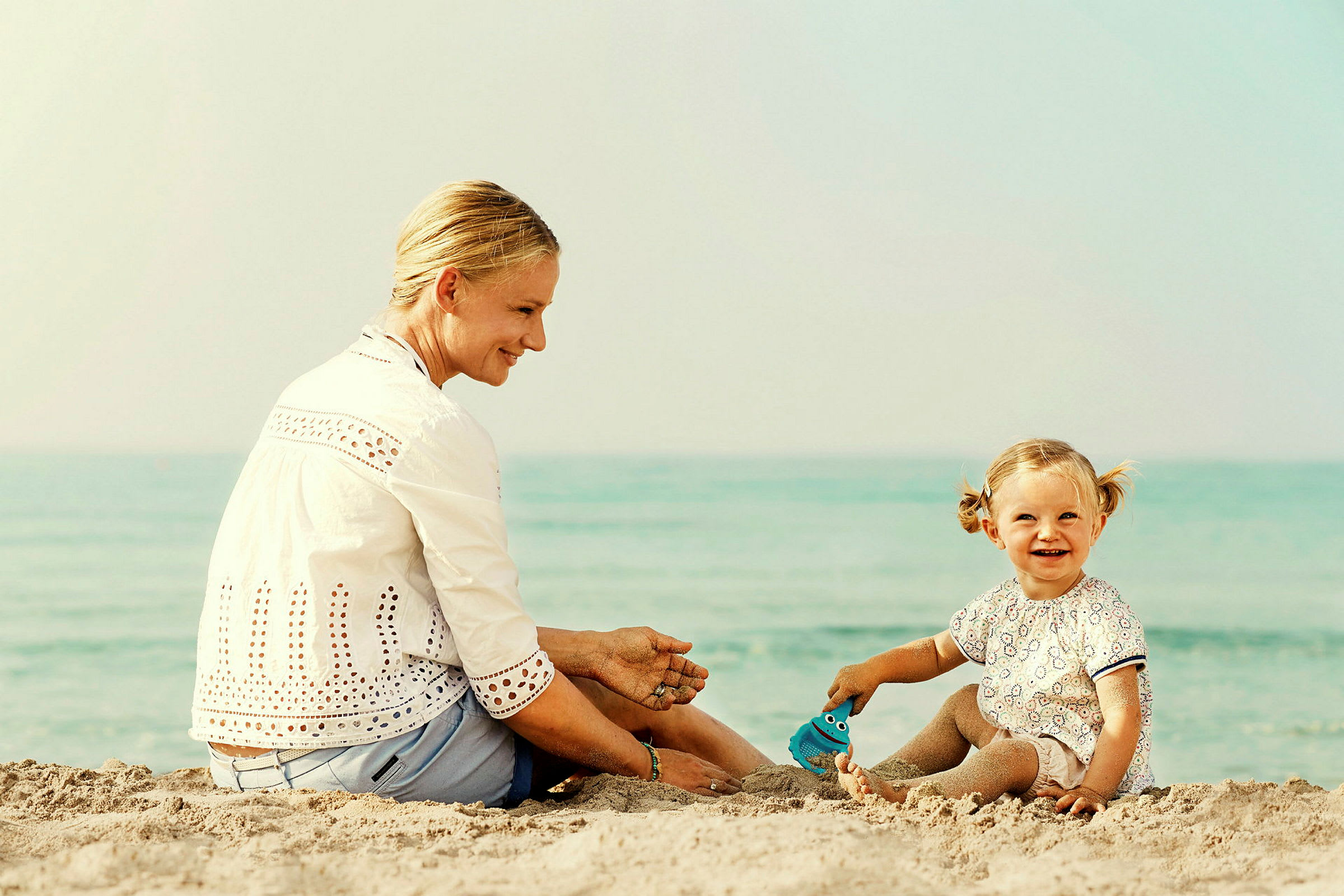 En person och ett barn sitter på en sandstrand nära vattnet. (AI-genererad text)